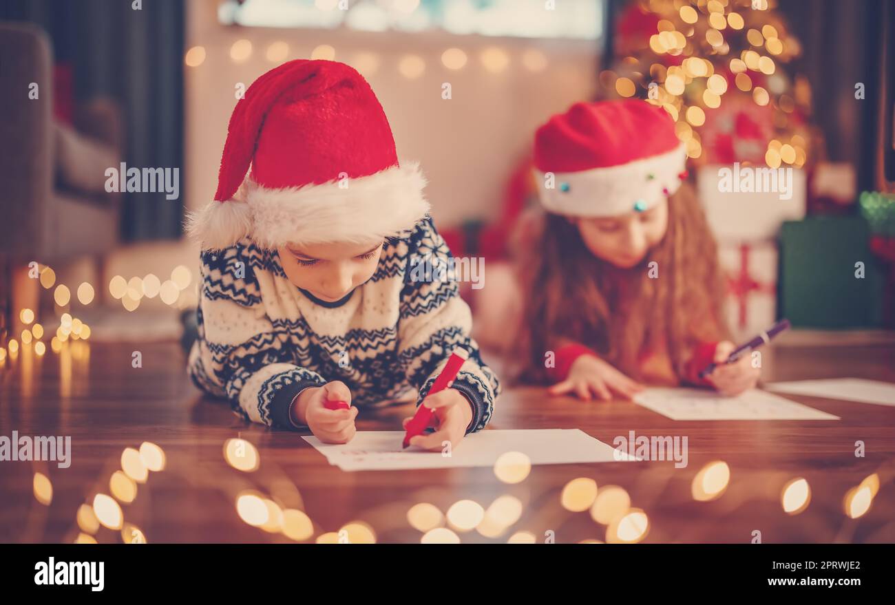 Kinder liegen drinnen auf dem Boden und schreiben Briefe für den Weihnachtsmann. Stockfoto