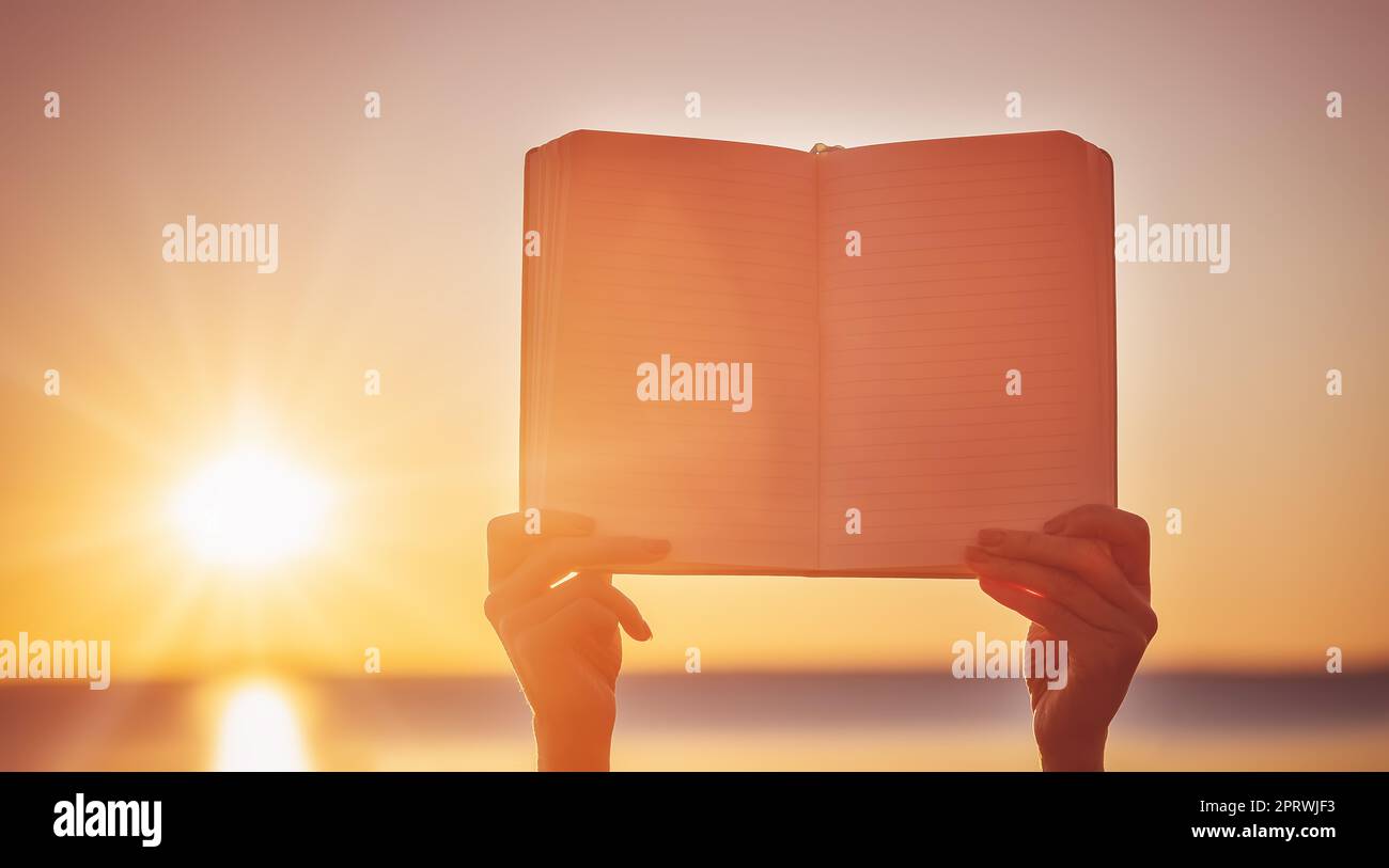 Menschliche Hände halten leere Lehrbücher im Freien auf den Sonnenuntergang Stockfoto