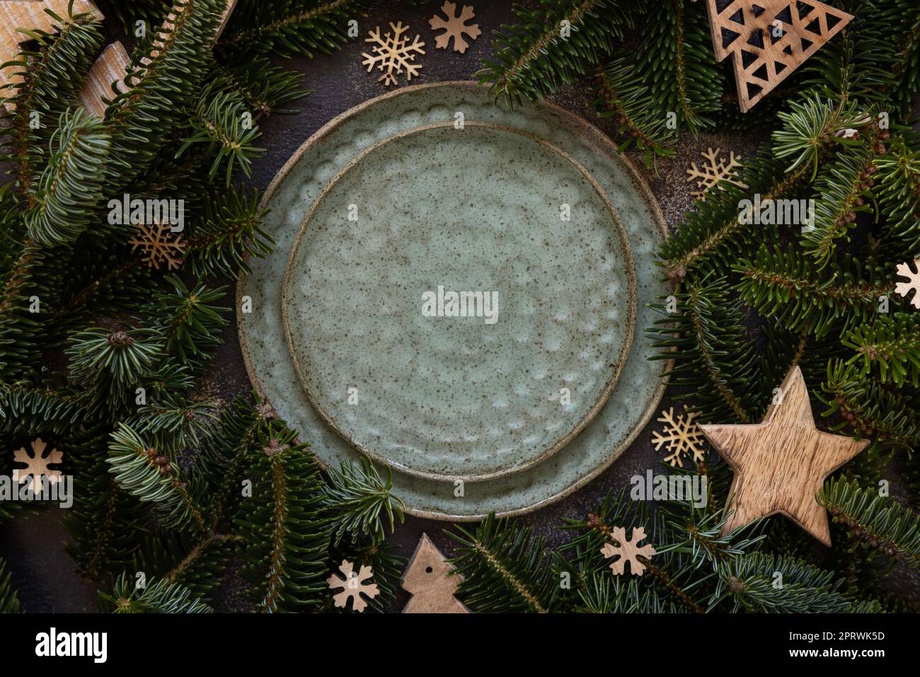 Festliche Tischgestaltung in der Nähe von Tannenbäumen und rustikale Weihnachtsdekorationen mit Blick auf den dunklen Tisch Stockfoto