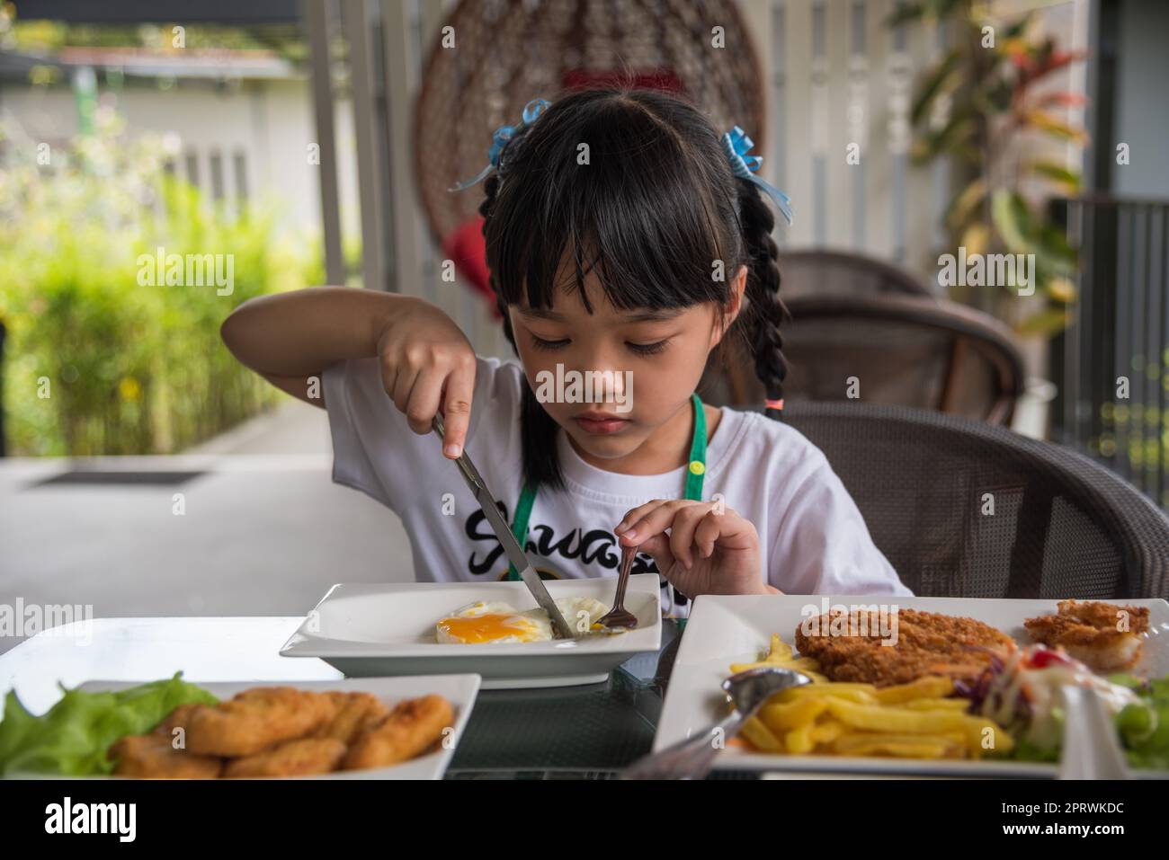 Kleine asiatische Mädchen essen Spiegelei auf Gericht am Tisch. Stockfoto