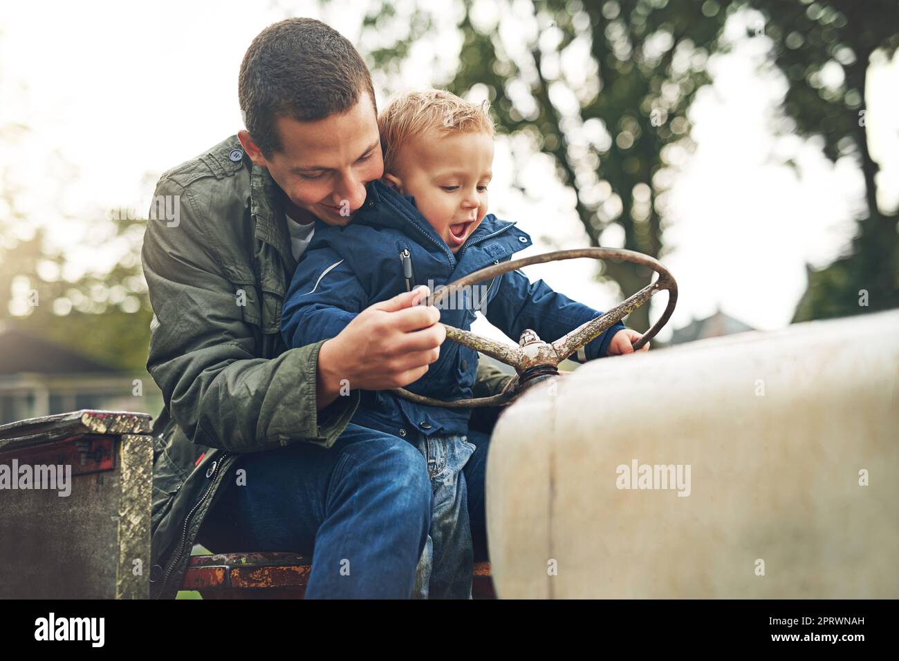 Halt dich gut fest. Ein Vater und sein kleiner Sohn, die draußen auf einem Traktor spielen Stockfoto