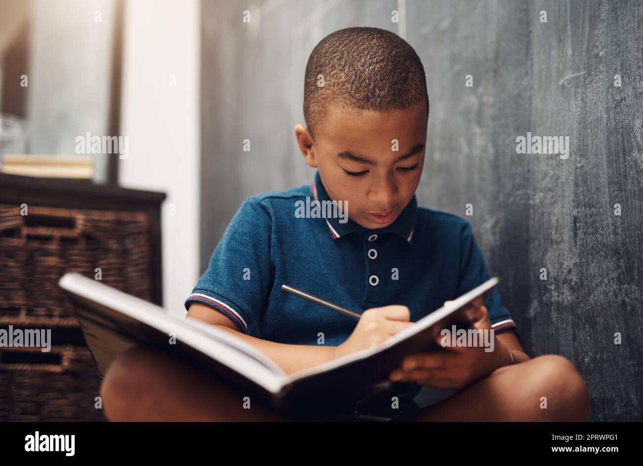 Der Beginn einer neuen Geschichte. Ein kleiner Junge, der zu Hause in einem Buch schreibt. Stockfoto