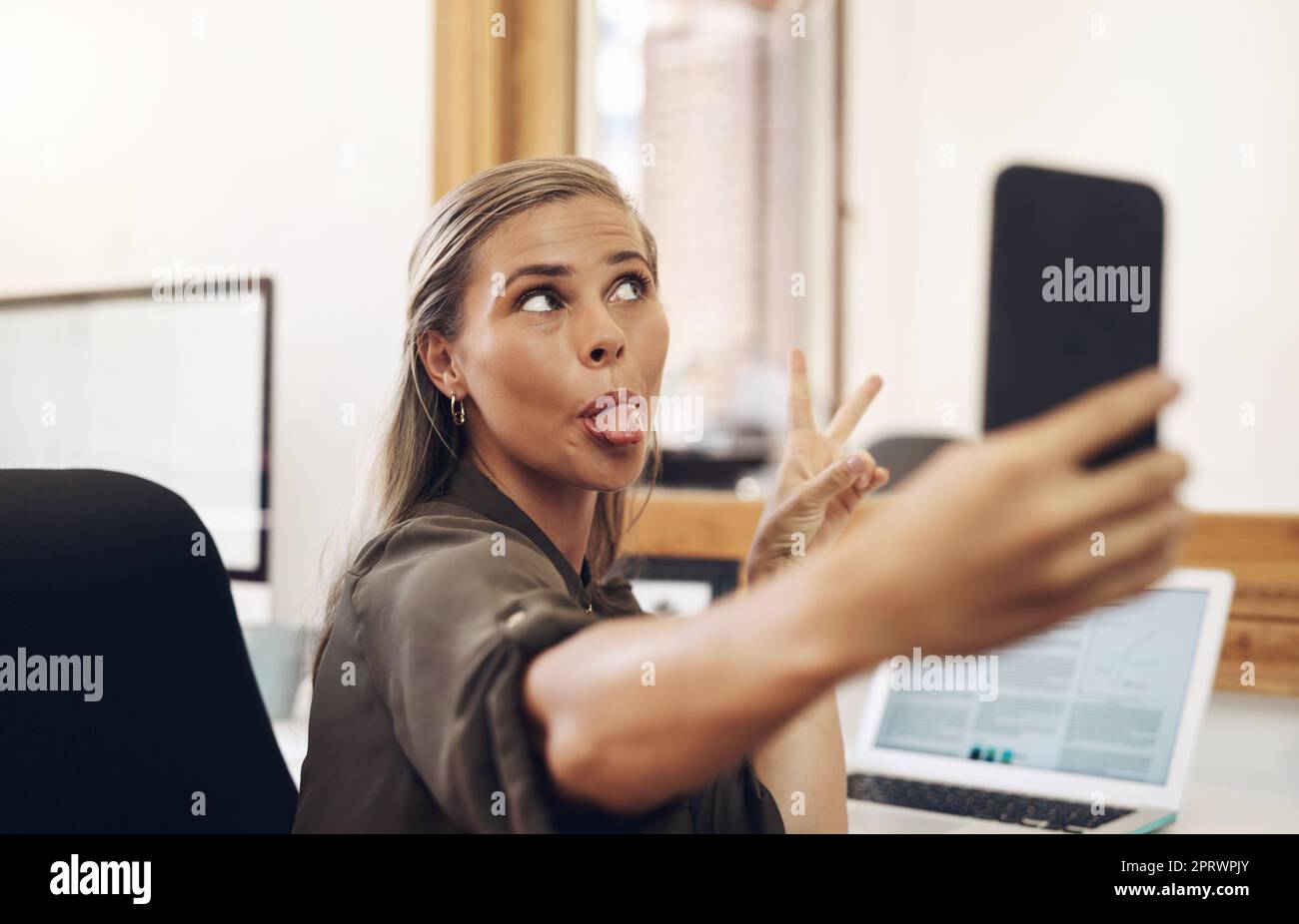 Nur ein bisschen Selfie-Sillness. Eine junge Geschäftsfrau ragt aus der Zunge, während sie Selfies in einem Büro macht. Stockfoto
