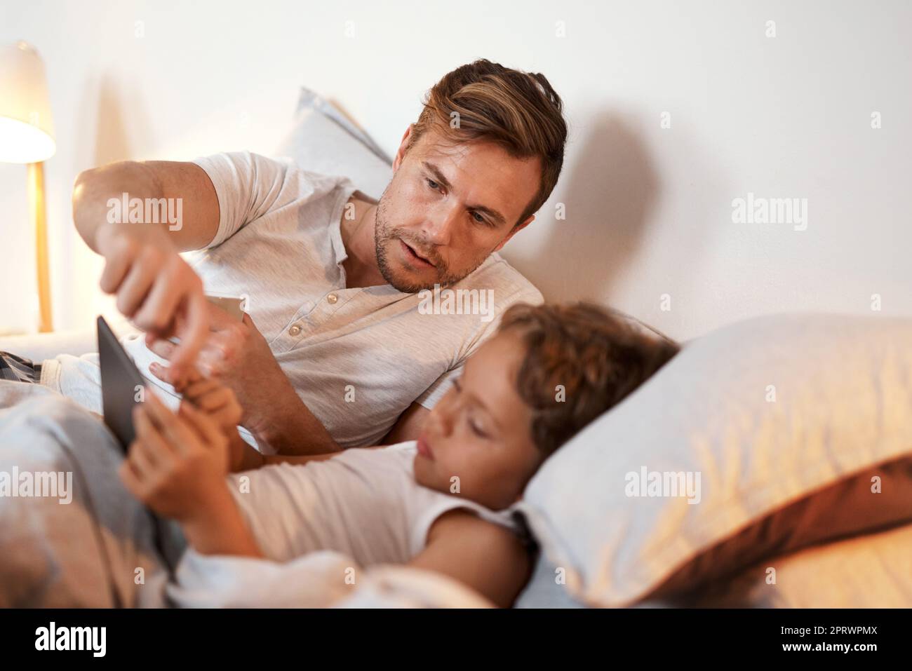 Mit E-Books macht das Schlafengehen viel mehr Spaß. Ein kleiner Junge nutzt ein digitales Tablet, während er mit seinem Vater im Bett liegt. Stockfoto