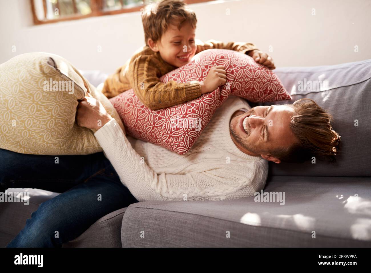 Ein Mann und sein kleiner Sohn, die zu Hause auf dem Sofa einen Kissenkampf führen. Stockfoto