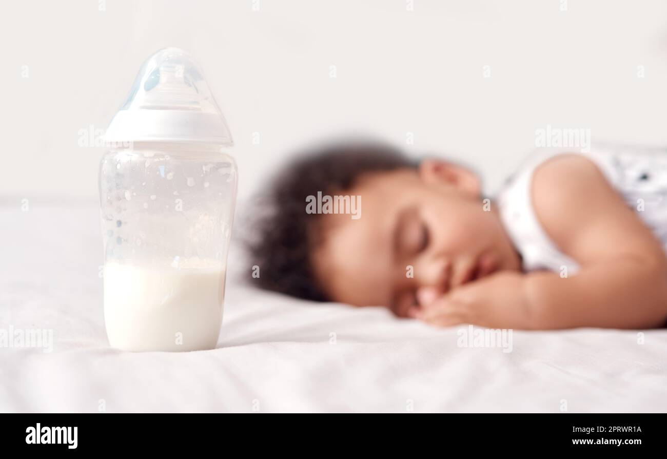 Das obligatorische Nickerchen nach einem Milchbusch. Ein entzückender Baby schläft mit seiner Flasche Milch auf dem Bett zu Hause. Stockfoto