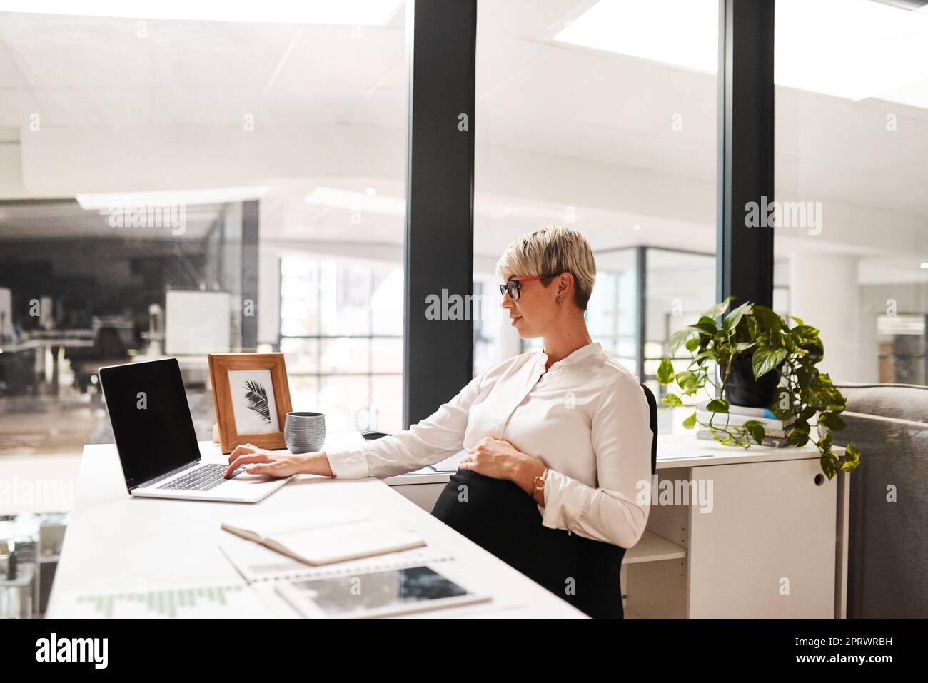 Große Pläne für die Zukunft ihres Geschäfts und ihrer Karriere. Eine schwanger Geschäftsfrau, die in einem Büro an einem Laptop arbeitet. Stockfoto
