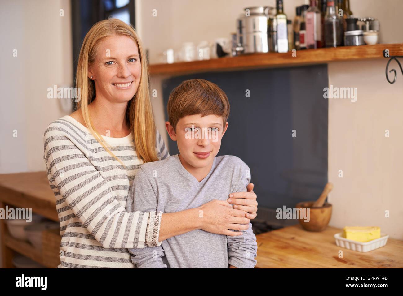 Widerstrebende Zuneigung eines fast-Teenagers. Ein beschnittenes Porträt einer glücklichen Mutter und eines Sohnes, die zu Hause in ihrer Küche stehen. Stockfoto