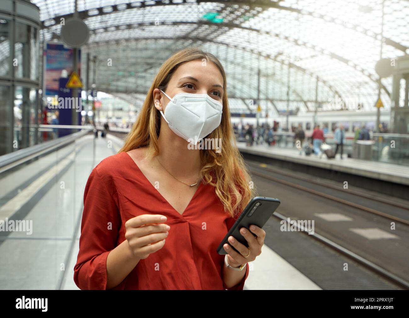 Reisende Frau trägt KN95 FFP2 Gesichtsmaske am Flughafen Bahnhof. Junge kaukasische Frau wartet auf den Shuttle-Zug zum Flughafen. Stockfoto