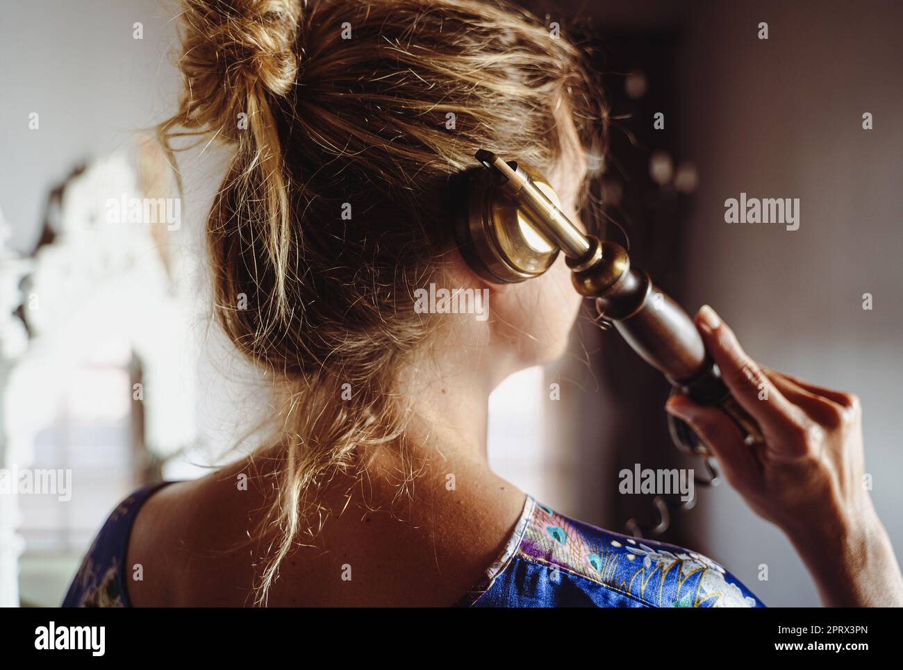 Porträt von einer Frau mit blondem Haar, die in intimer Innenraumbeleuchtung über ein altmodisches Telefon spricht Stockfoto