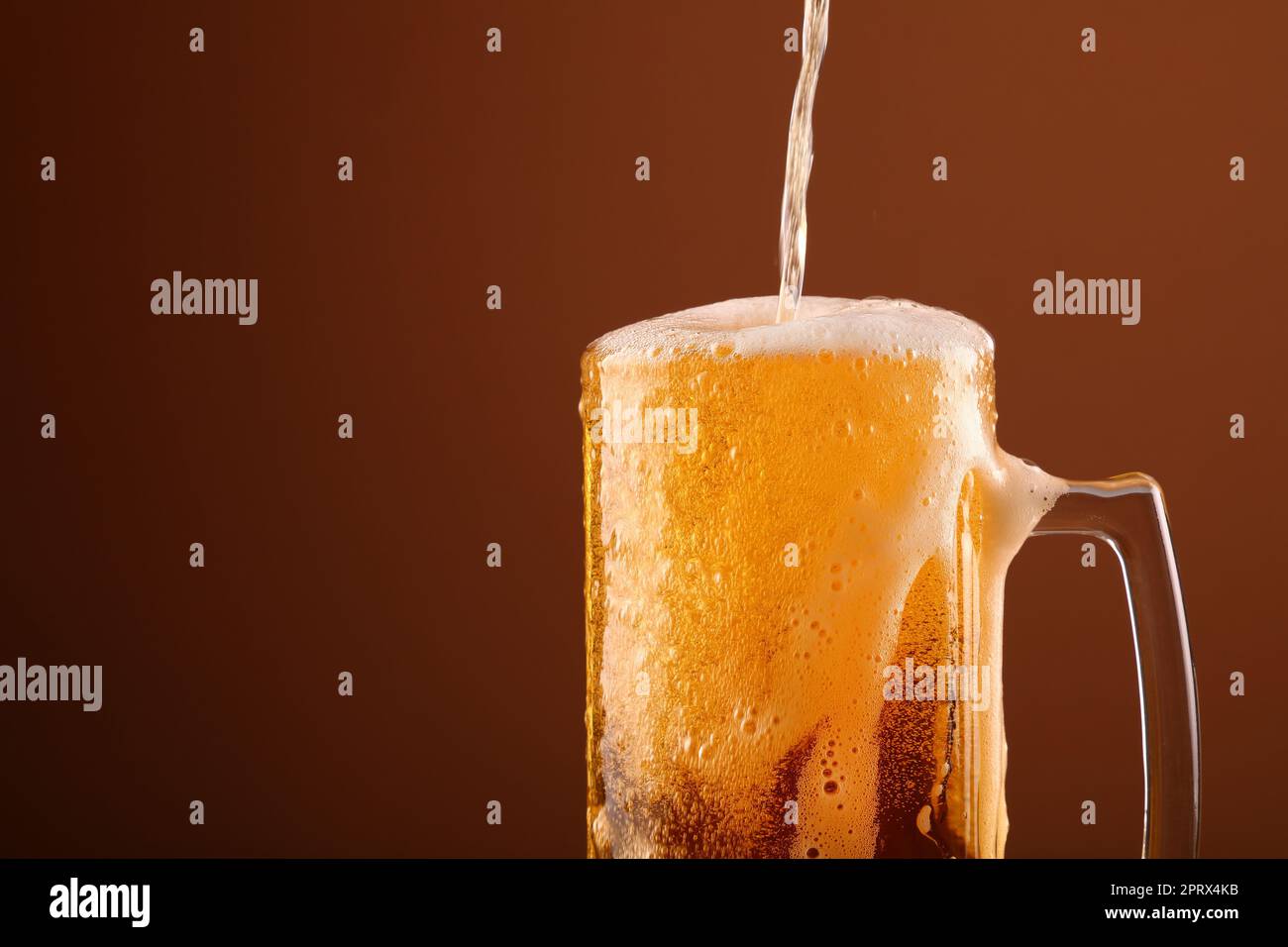 Nahaufnahme Gießen schaumig Bier in Glas über braun Stockfoto