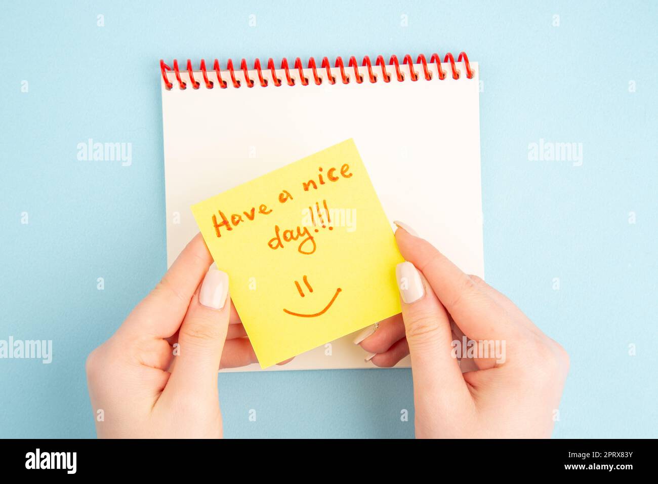 Spiralnotizbuch mit Draufsicht, weibliche Hand, gelbes Notizpapier mit schönen Tagesausdrücken auf blauem Hintergrund Stockfoto