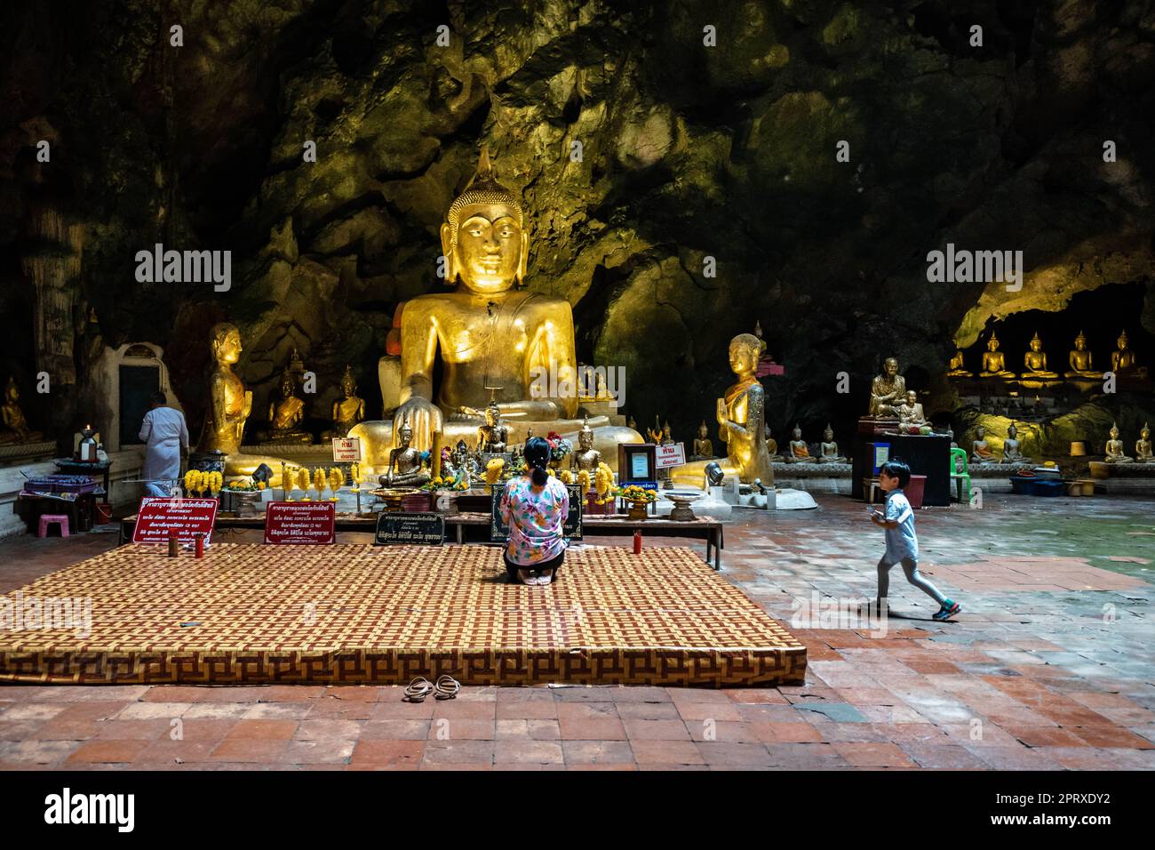 Phetchaburi, Thailand. 26. April 2023. Eine treue thailändische Mutter betet mit ihrem Sohn vor der größten Buddha-Statue der Tham Khao Luang Höhle in der Provinz Phetchaburi. Die Tham Khao Luang Höhle, eine Höhle mit Stalaktiten, einer der beeindruckendsten Höhlenschreine Thailands, ist voller Buddha-Bilder und war schon immer ein wichtiger Meditationsort, auch nicht weit von Bangkok entfernt, sie ist eines der meistbesuchten Touristenziele von Thais und ausländischen Reisenden. Kredit: SOPA Images Limited/Alamy Live News Stockfoto