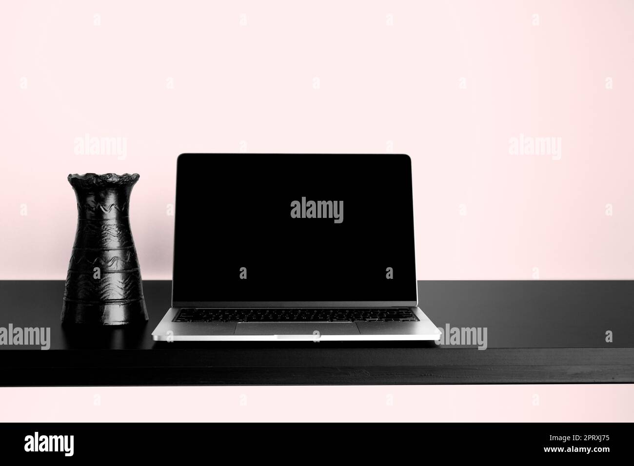 Laptop-Modell auf schwarzem Holztisch mit wechselbarem Desktophintergrund. Mit schwarzer Vase und pinkfarbenem Hintergrund. Stockfoto