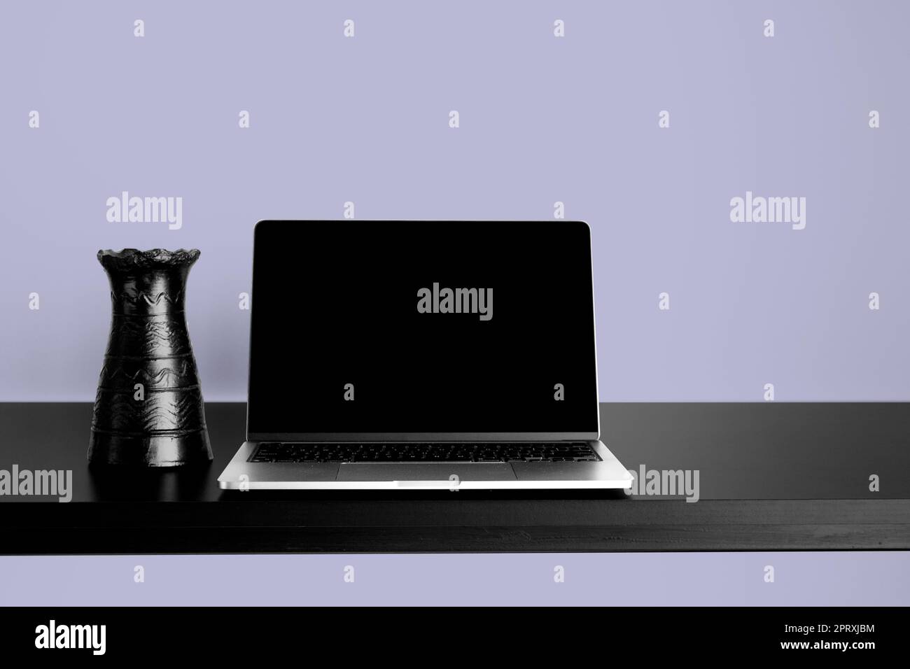 Laptop-Modell auf schwarzem Holztisch mit wechselbarem Desktophintergrund. Mit schwarzer Vase und lila Hintergrund. Stockfoto