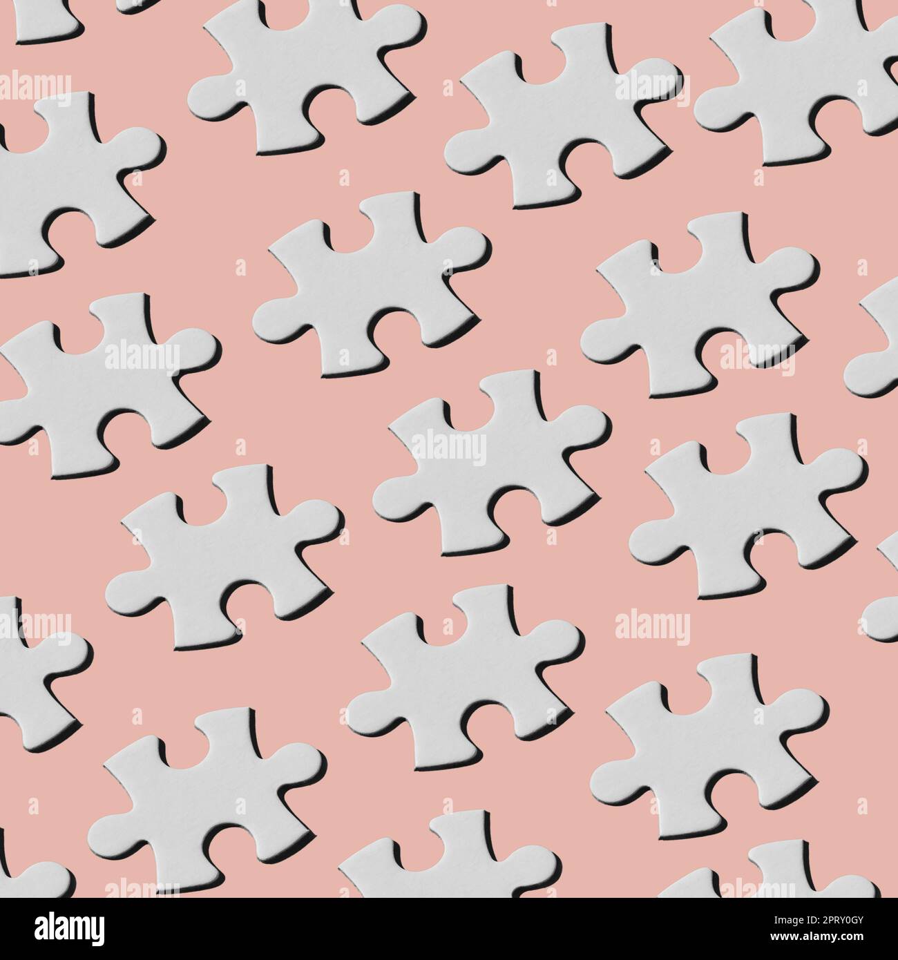 Ein Muster aus weißen Puzzleteilen, die in verschiedenen Linien auf einem blassrosa Hintergrund angeordnet sind Stockfoto