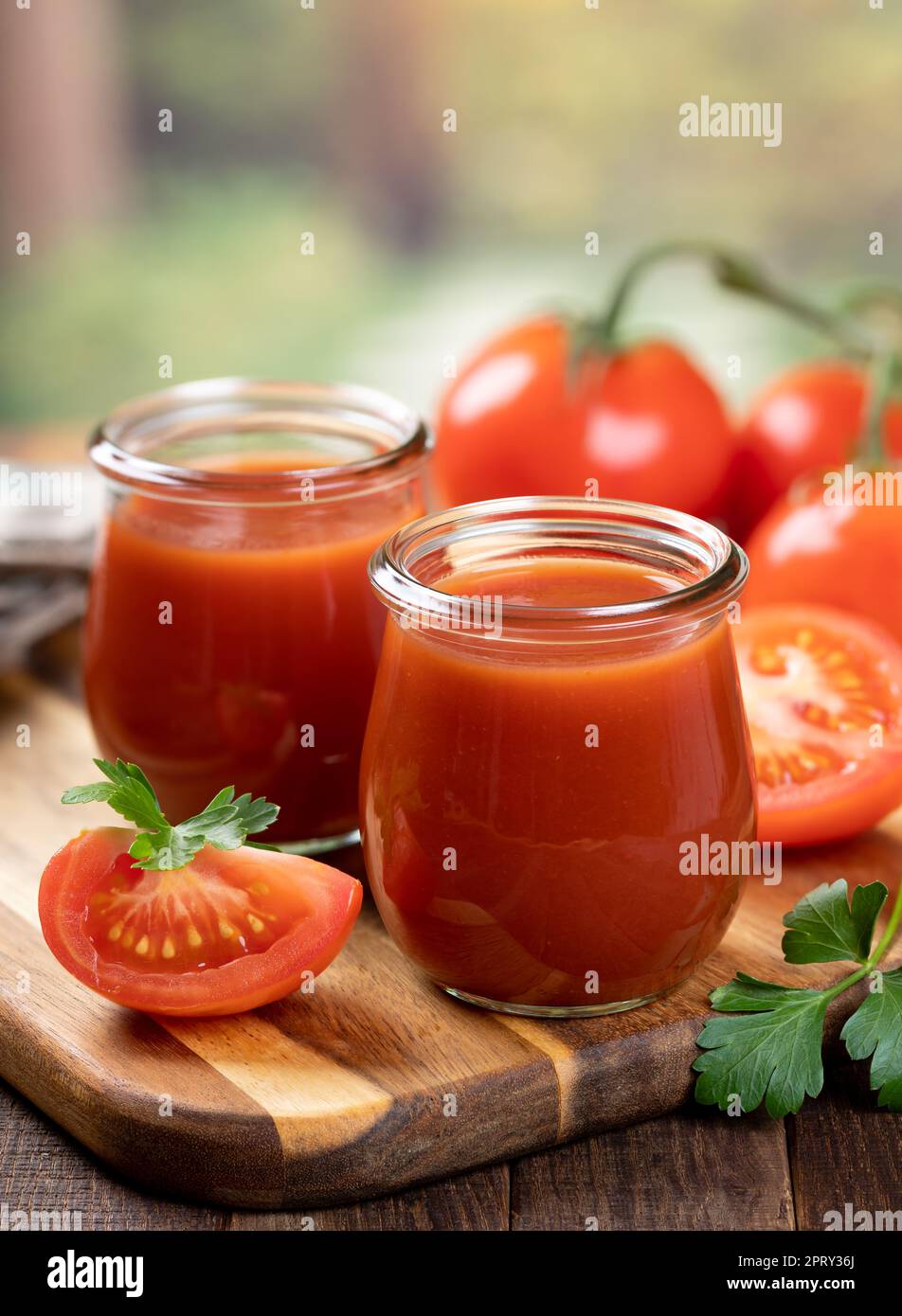 Tomatensaft in Glasgefäßen mit frischen Tomatenscheiben auf Holzbrett mit Außenhintergrund Stockfoto