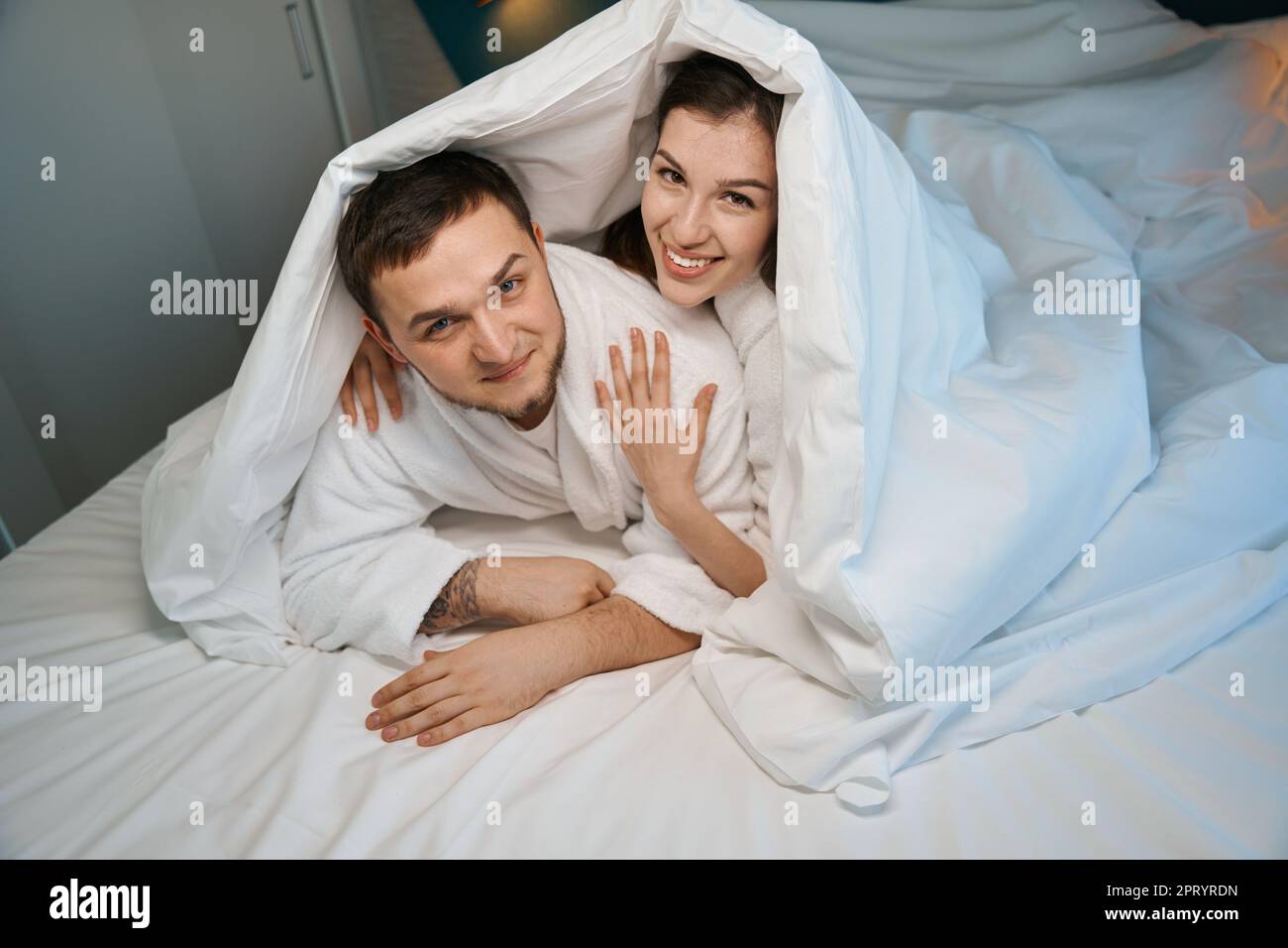 Glückliches junges Paar, das sich auf einem großen Bett umarmt Stockfoto