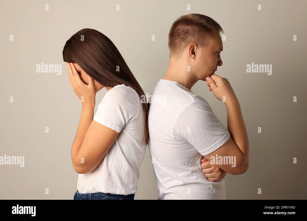 Unglückliches junges Paar, das sich vor hellem Hintergrund den Rücken zudreht Stockfoto