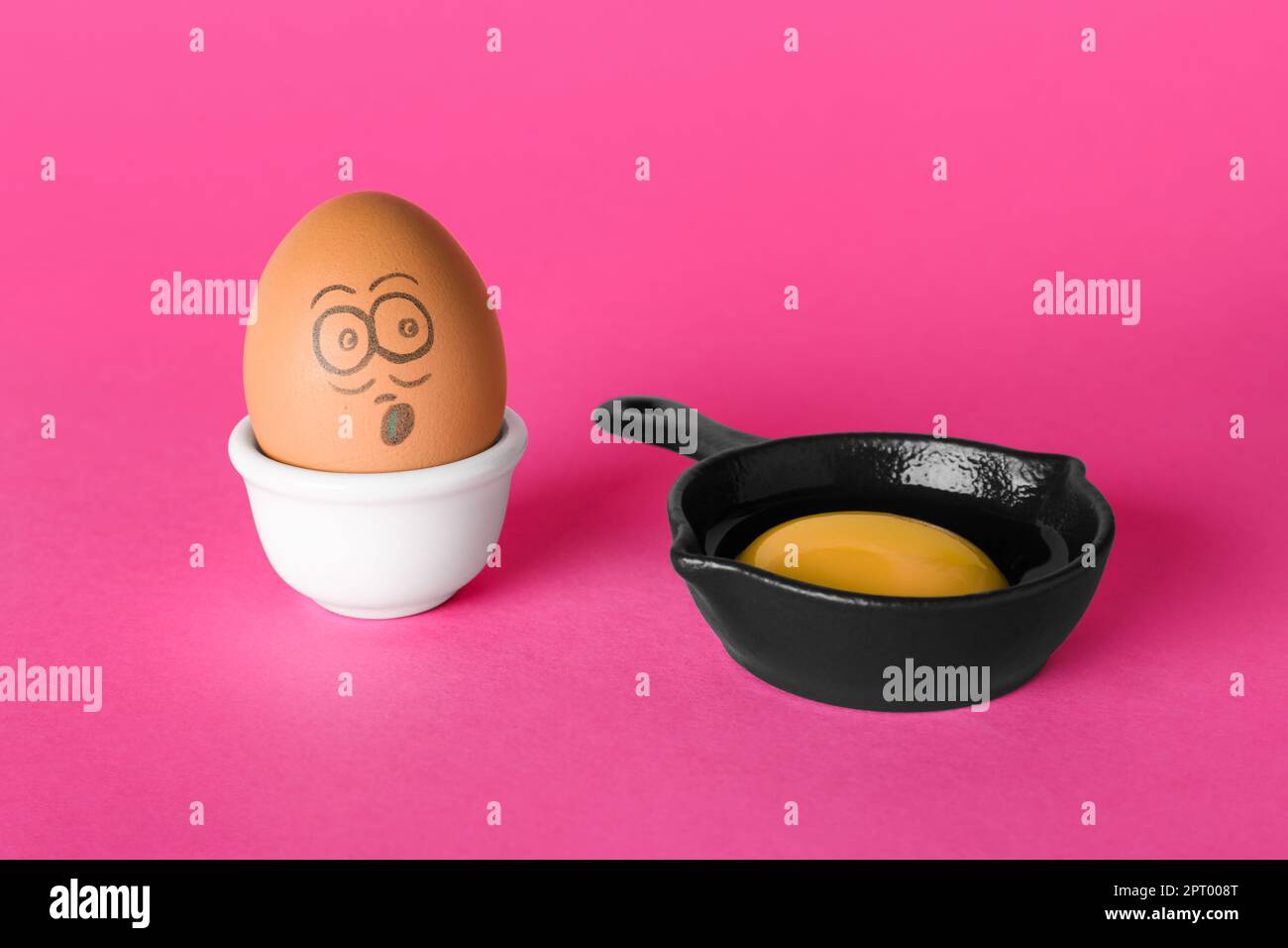 Ei mit gezogenem, geschocktem Gesicht und Eigelb in kleiner Bratpfanne auf pinkfarbenem Hintergrund Stockfoto