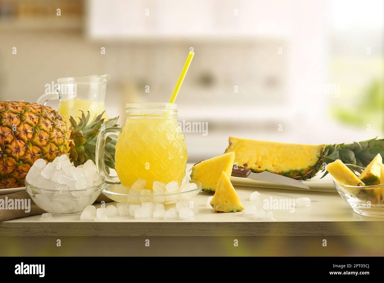 Ein Glas Ananasgetränk mit Eis auf dem Tisch mit zerdrücktem Eis und Obst und Küchenhintergrund. Vorderansicht. Horizontale Zusammensetzung. Stockfoto