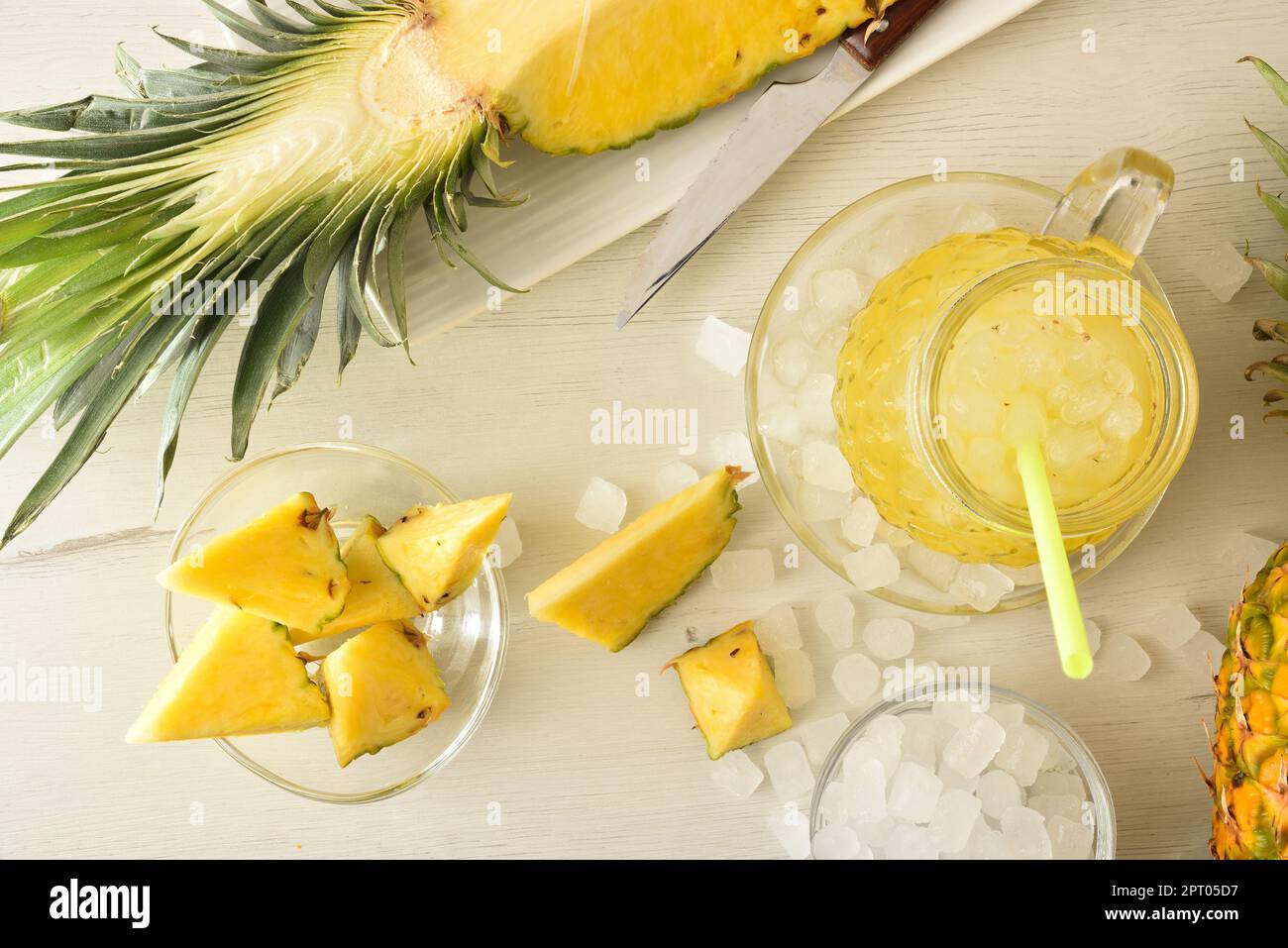 Frisch zubereitetes Ananas-Erfrischungsgetränk mit viel Eis auf einer hölzernen Küchenbank mit Obst und einer Schüssel mit Eis drum herum. Draufsicht. Horizontale Kombi Stockfoto