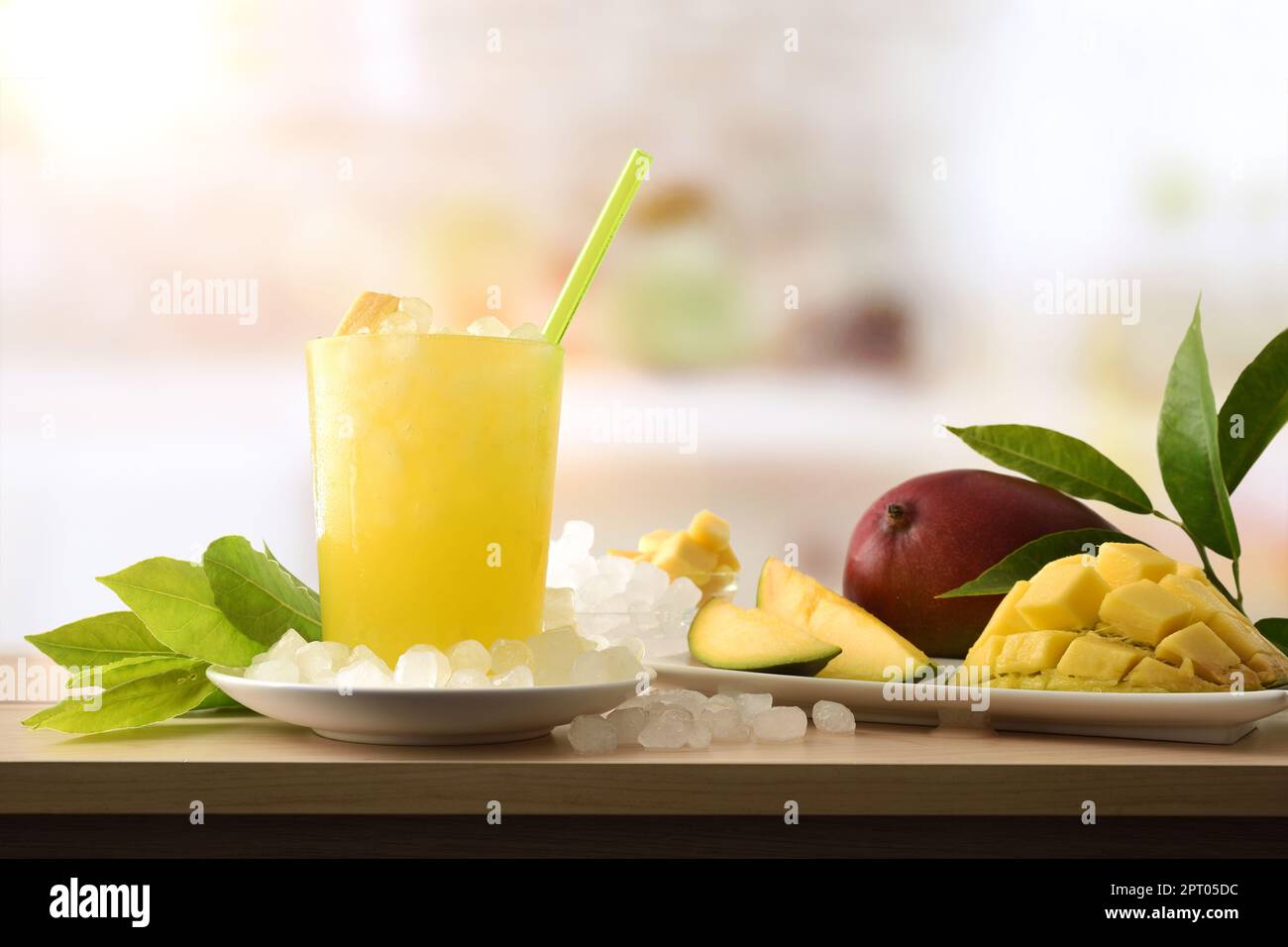 Detail eines Mango-Erfrischungsgetränks mit viel Eis auf einer hölzernen Küchenbank mit Obst und einer Schüssel mit Eis drum herum. Vorderansicht. Horizontale Zusammensetzung. Stockfoto