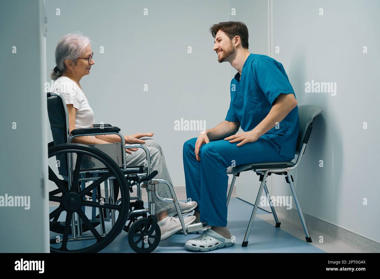 Der Mann in der medizinischen Uniform kommuniziert mit dem älteren Patienten im Rollstuhl Stockfoto