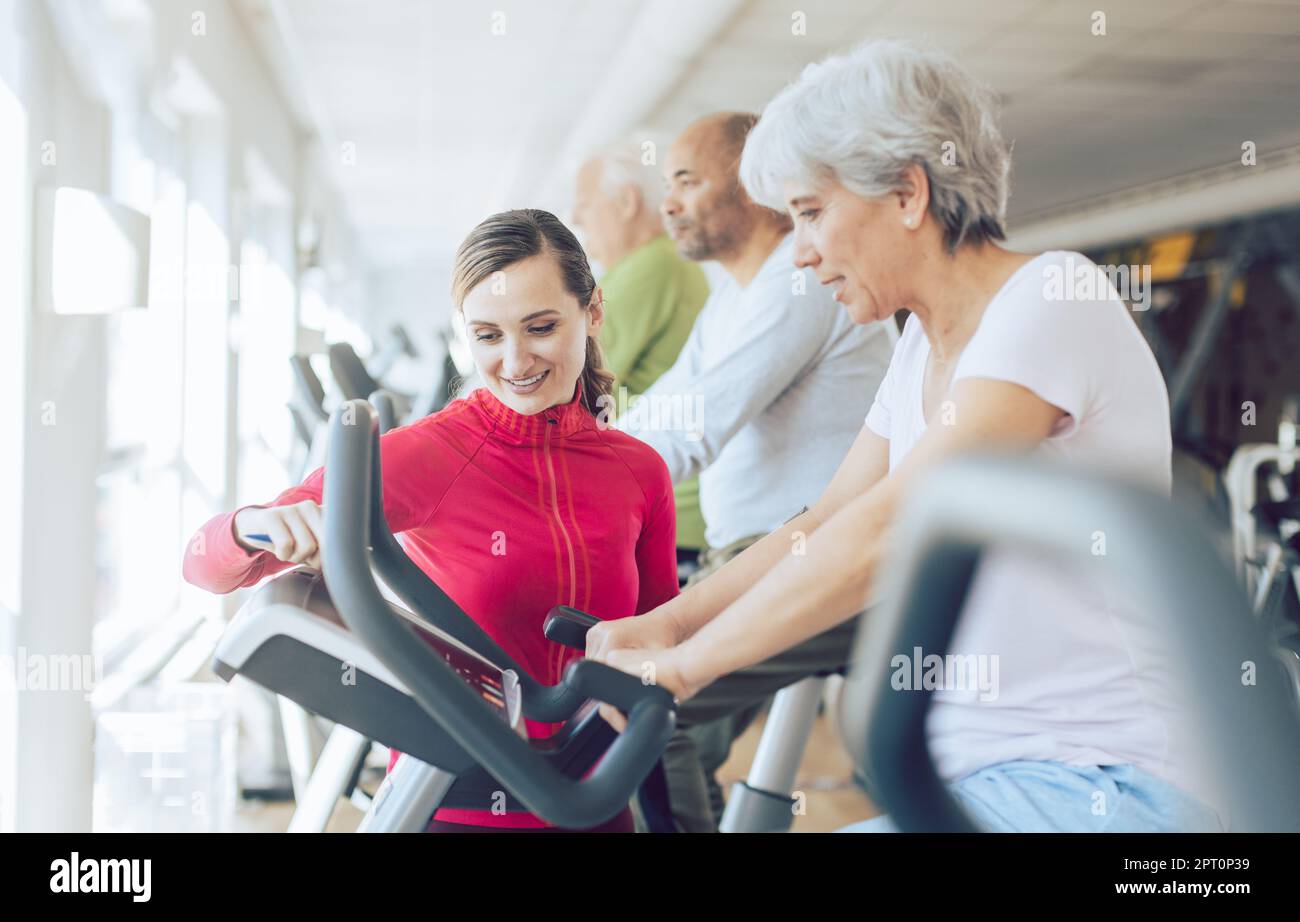 Fitnesstrainer im Fitnessstudio hilft älteren Menschen beim Cardio-Bike-Training Stockfoto