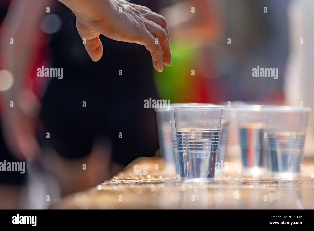 Die Hand eines Marathonläufers greift nach einem Plastikbecher mit Wasser Stockfoto