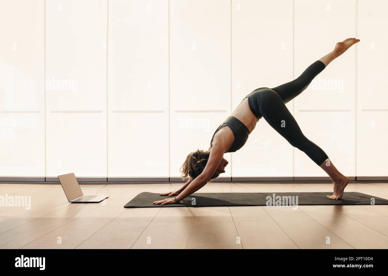 Reife Frau, die während eines Online-Yogakurses zu Hause eine Hundeübung macht. Seniorin streckt ihren Körper auf einer Trainingsmatte. Frau folgt einem Stockfoto