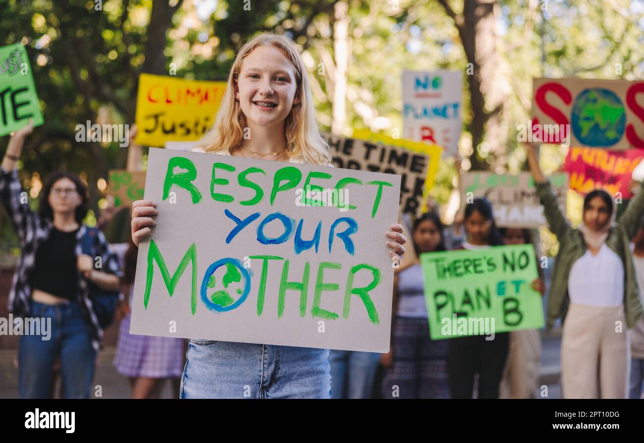 Fröhlicher Teenager, der in die Kamera lächelt, während er einen marsch gegen die globale Erwärmung führt. Gruppe multiethnischer Jugendaktivisten, die gegen das Klima protestieren Stockfoto
