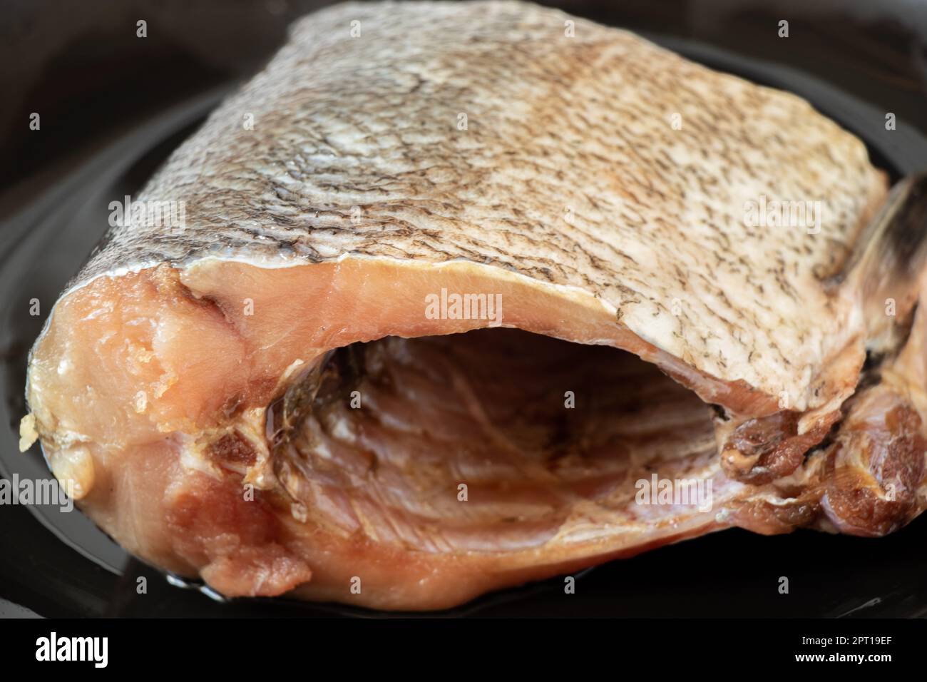 Ein rohes Stück Silberkarpfenfisch liegt auf einem schwarzen Teller Stockfoto