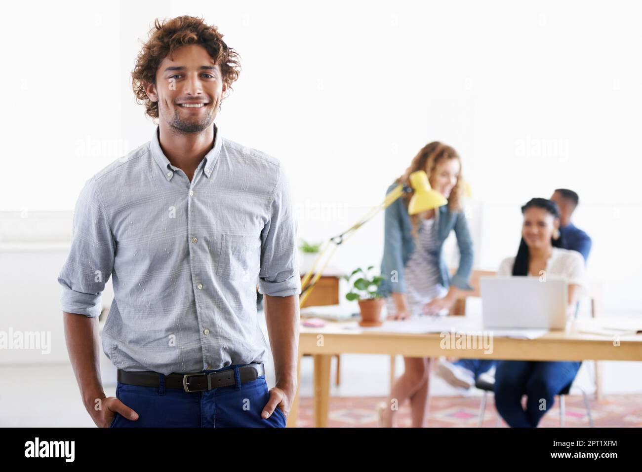 Ja, es ist ein toller Arbeitsplatz. Porträt eines jungen Büromitarbeiters mit seinen Kollegen im Hintergrund Stockfoto