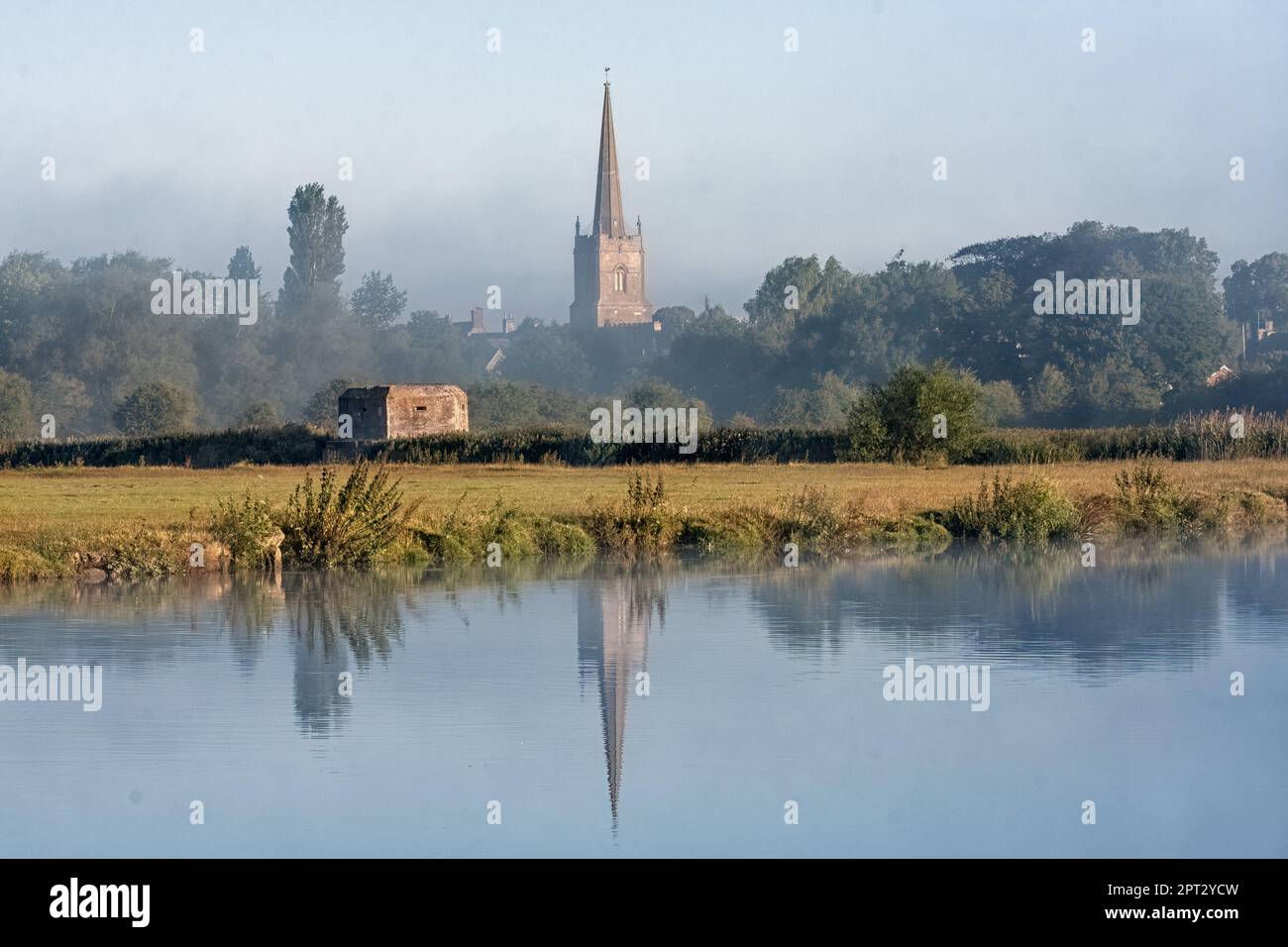 LECHLADE, GLOUCESTERSHIRE, Großbritannien - 04. JULI 2008: Blick über die Themse in Richtung St. Lawrence Kirche in sanftem Morgenlicht mit Reflexion Stockfoto