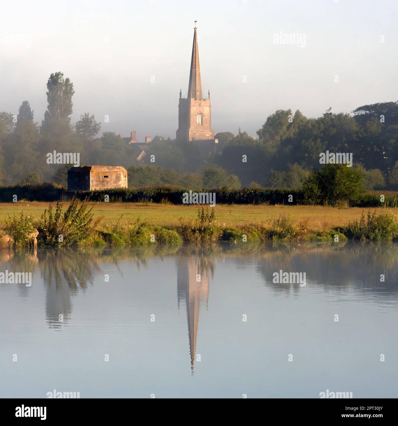 LECHLADE, GLOUCESTERSHIRE, Großbritannien - 04. JULI 2008: Blick über die Themse in Richtung St. Lawrence Kirche in sanftem Morgenlicht mit Reflexion Stockfoto