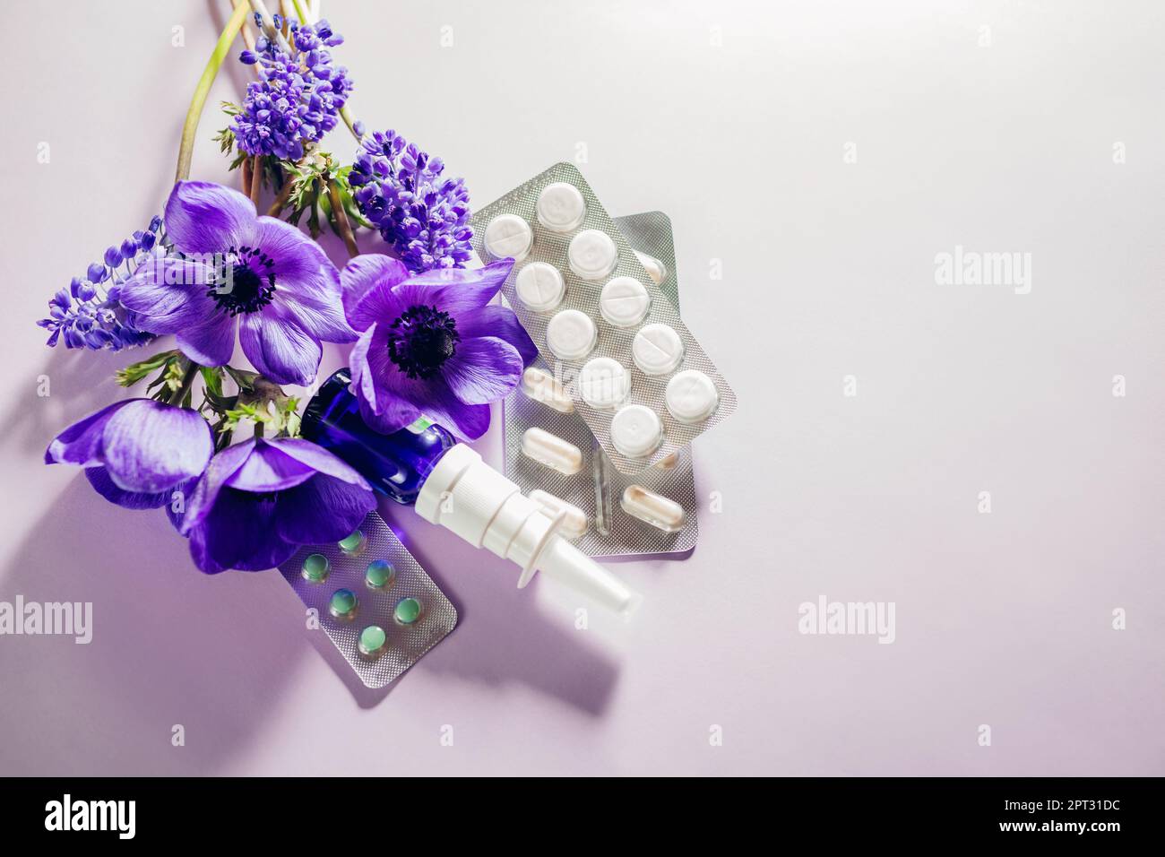 Saisonale Frühjahrsallergie im Hintergrund. Pillen und Nasenspray lagen flach mit lila Blüten. Pollenallergen. Antihistaminika. Leerzeichen Stockfoto