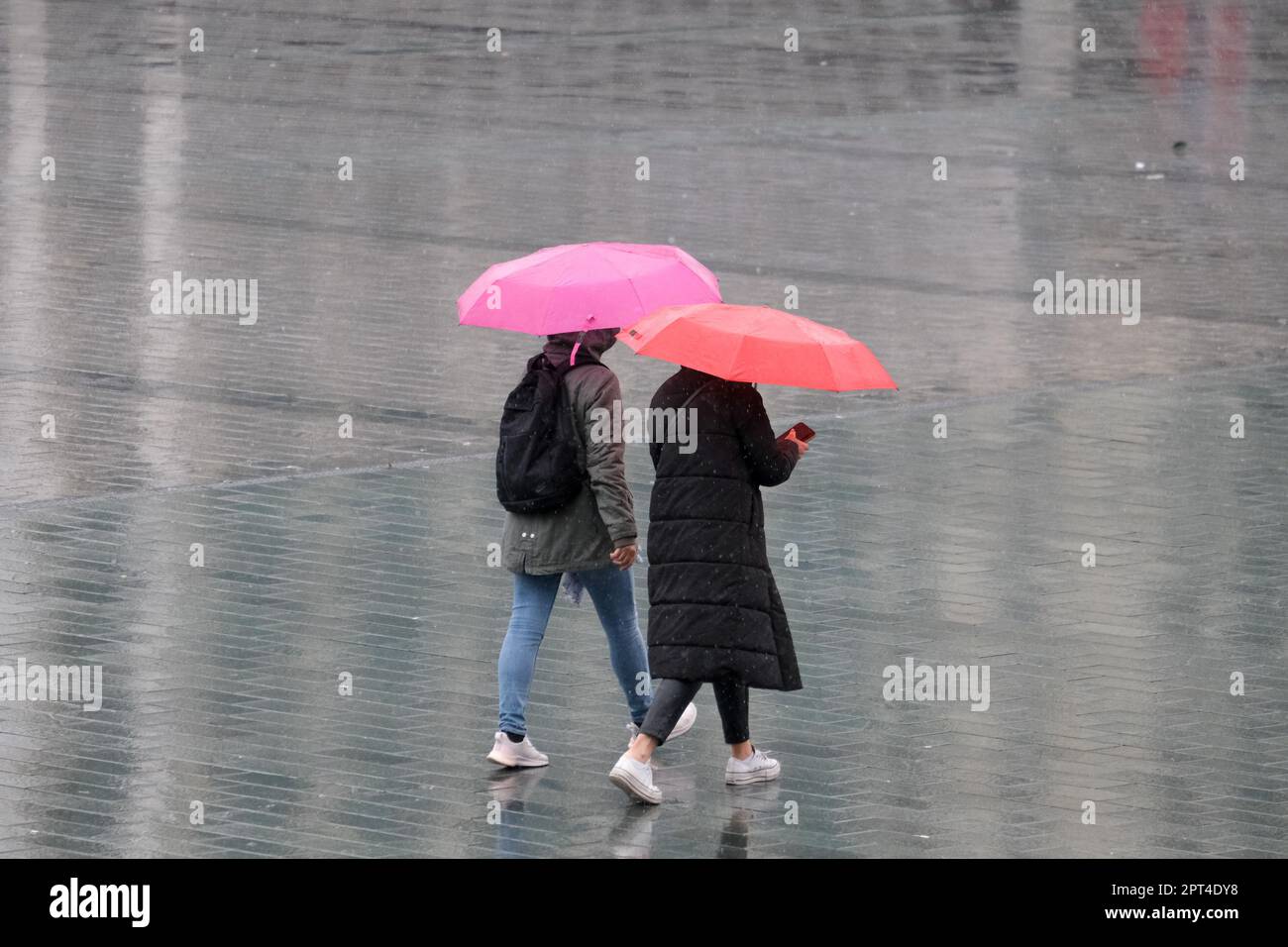 Zwei Frauen mit pinkfarbenem orangefarbenem Regenschirm unter Regen, die vom hinteren Teil aus laufen und kein Gesicht haben. Farbenfroher Regenschirm im Herbst. Selektiver Fokus. Stockfoto
