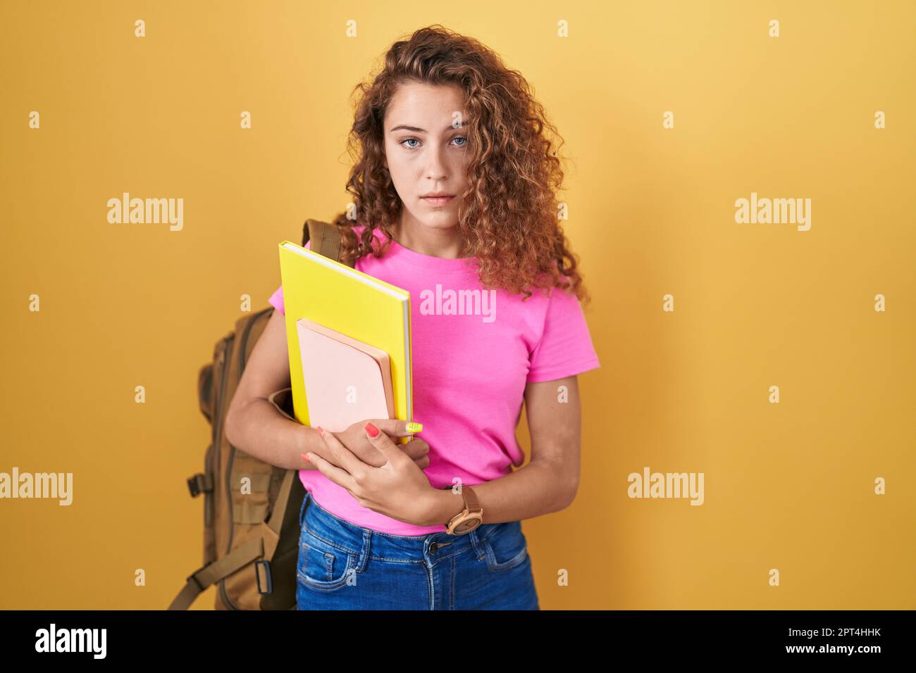Junge weiße Frau, die einen Studentenrucksack trägt und Bücher in der Hand hält, schläfrig und müde aussieht, erschöpft wegen Müdigkeit und Kater, faule Augen am Morgen Stockfoto