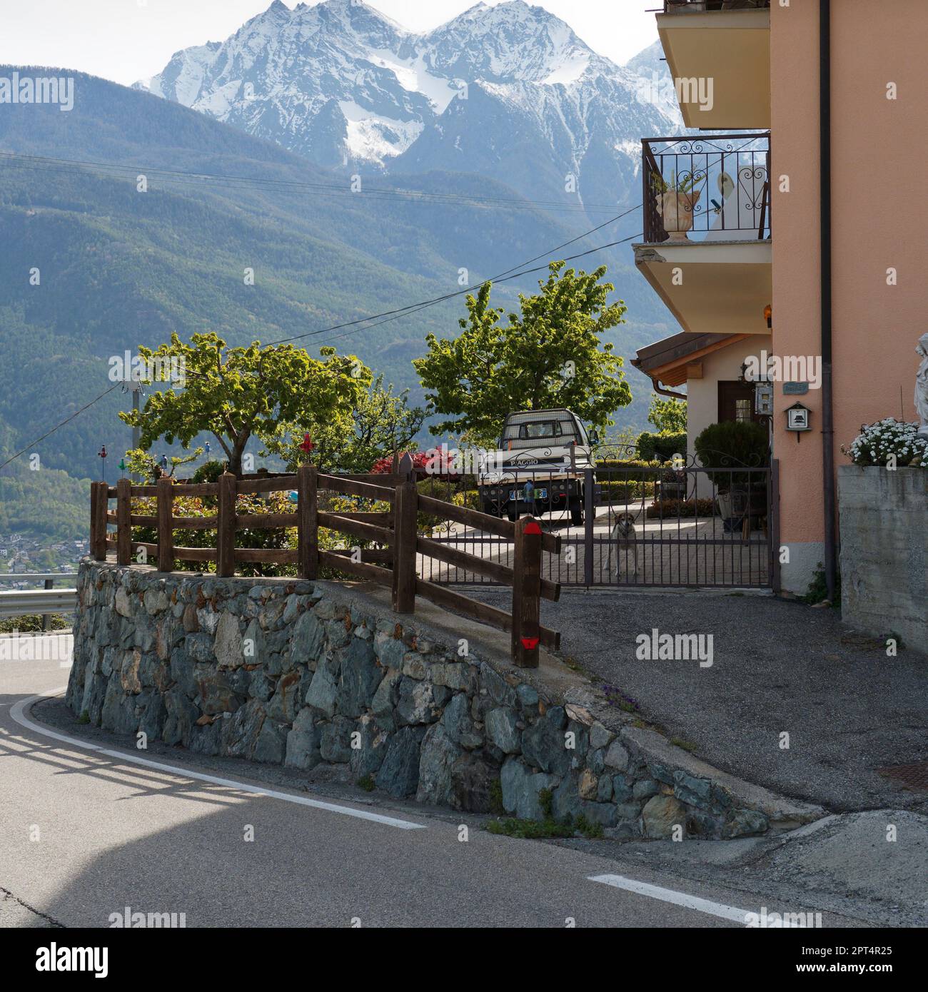 Haus mit Hochsteineinfahrt mit Ape-Auto, Hund und Balkon. Schneebedeckte alpine Berge dahinter. Aosta Valley, NW Italien Stockfoto