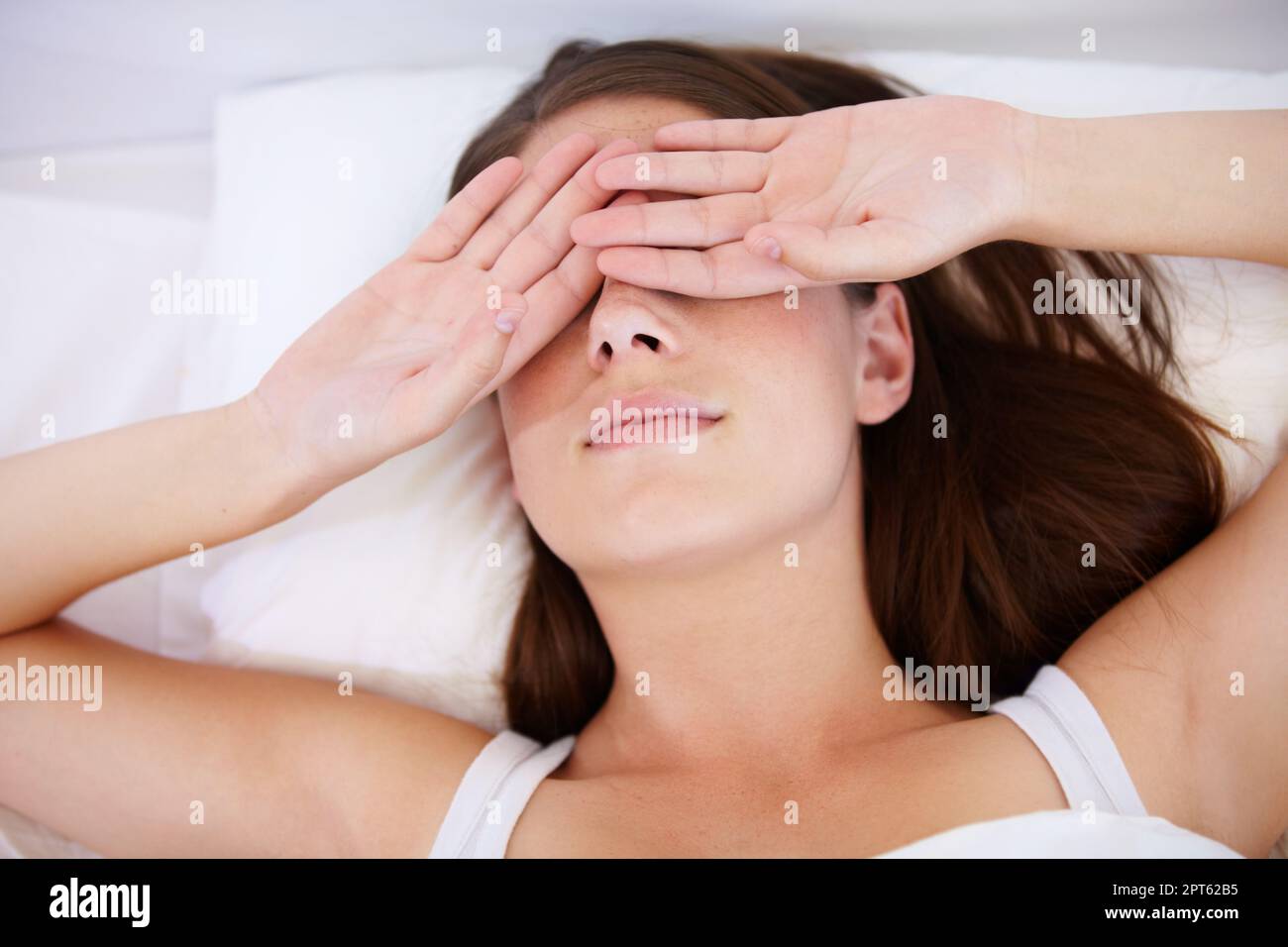 Ich brauche mehr Schlaf. Eine junge Frau lag im Bett mit den Händen über den Augen Stockfoto