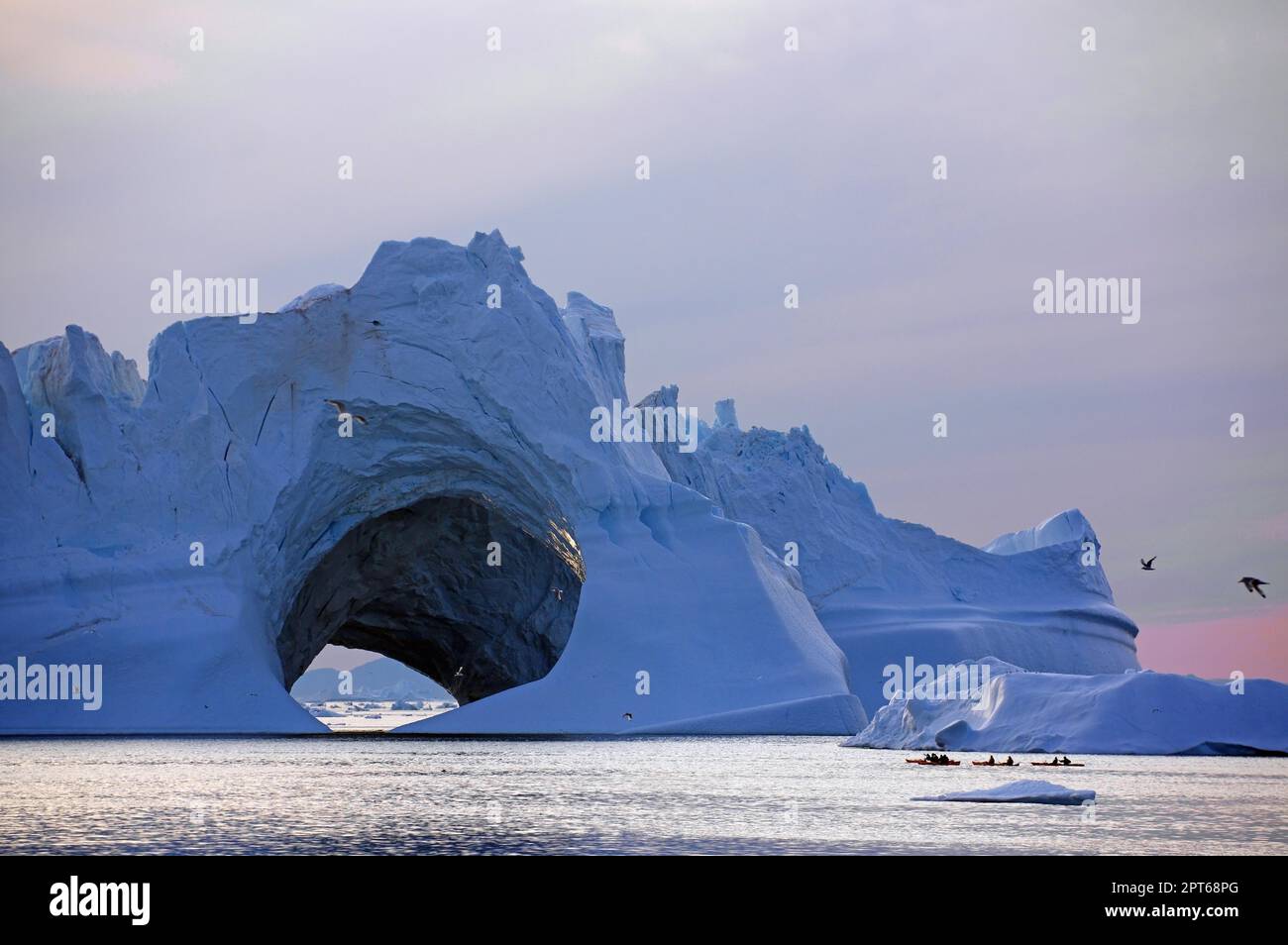 Kajakfahrer vor dem riesigen Eisberg, Eishöhle, Mitternachtssonne, Ilulissat, Disko Bay, Dänemark, Grönland Stockfoto