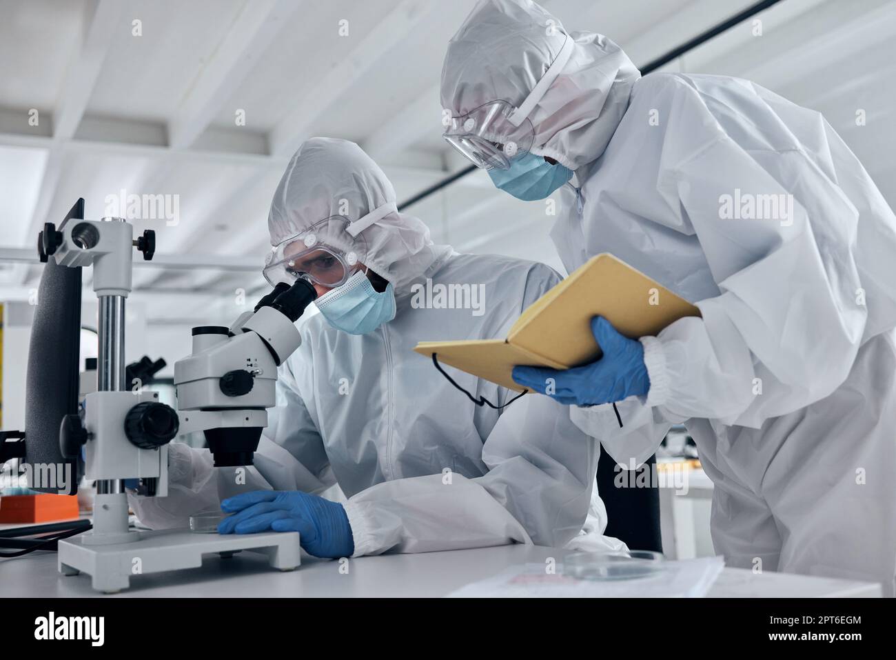 Wissenschaftlerteam, covid-Forschung und Mikroskop mit Team, das Notizen oder Ergebnisse während der Analyse einer Probe in einem Wissenschafts- und medizinischen Labor schreibt. Medizinisch Stockfoto