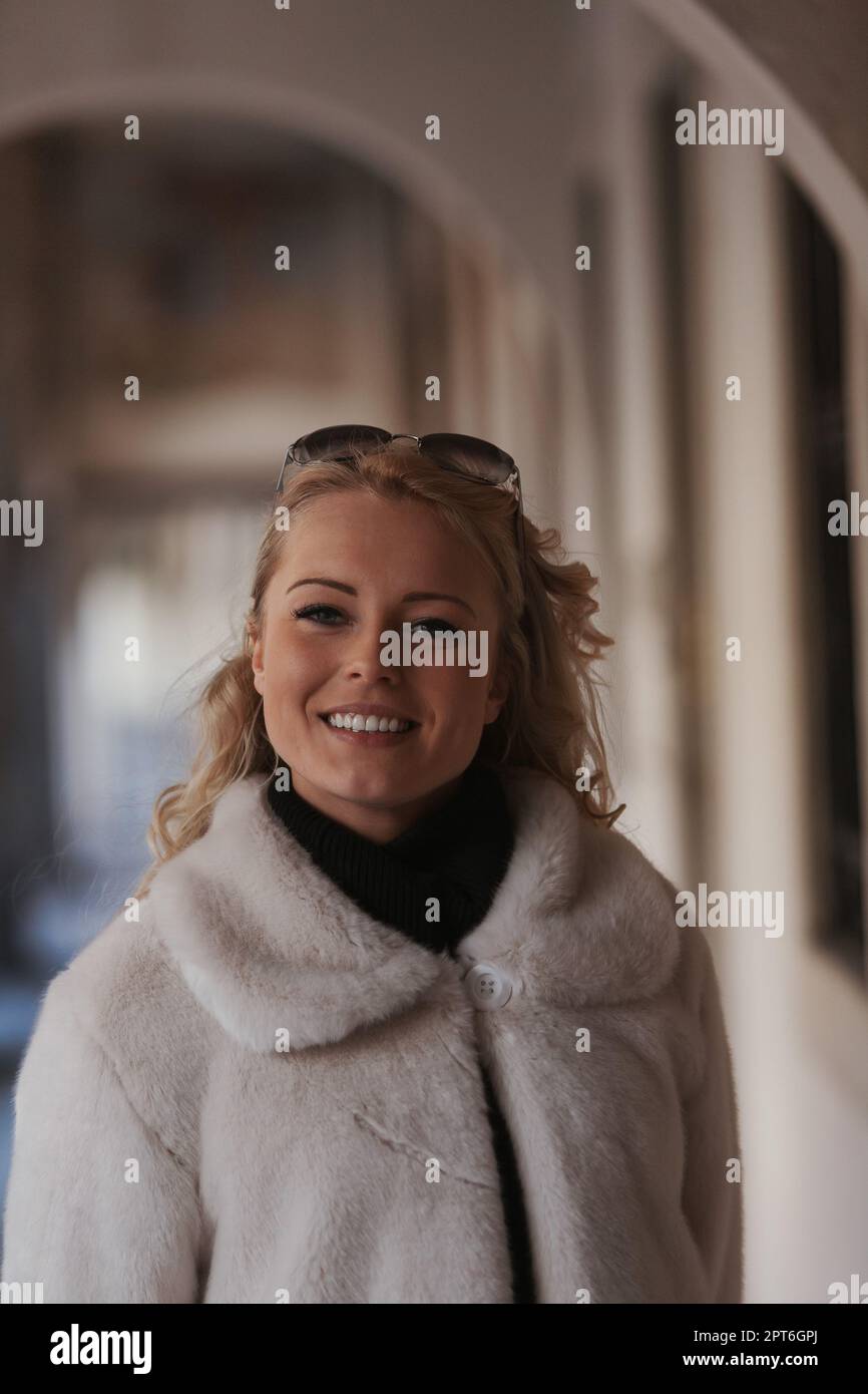 Eine blonde Frau besichtigt eine historische europäische Stadt voller kopfsteingepflasterter Straßen, Torbögen, Marmor und mittelalterlicher oder gotischer Elemente Stockfoto