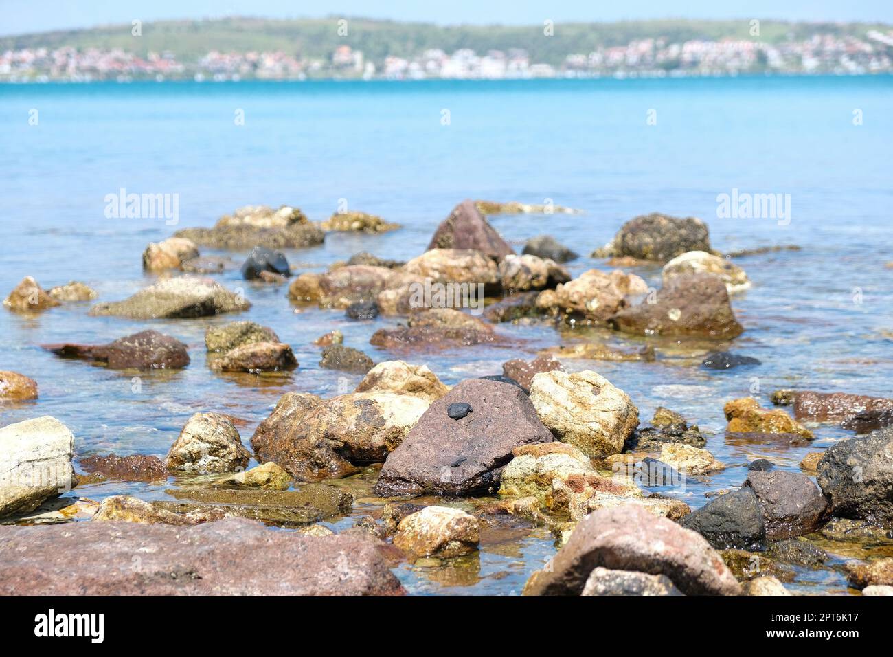 Blick vom Boden aus auf den Meeresstrand aus Kieselsteinen mit weitem Horizont und Stadt. Hintergrundkonzept für den Sommerstrand am Meer. Niemand am Strand. Stockfoto