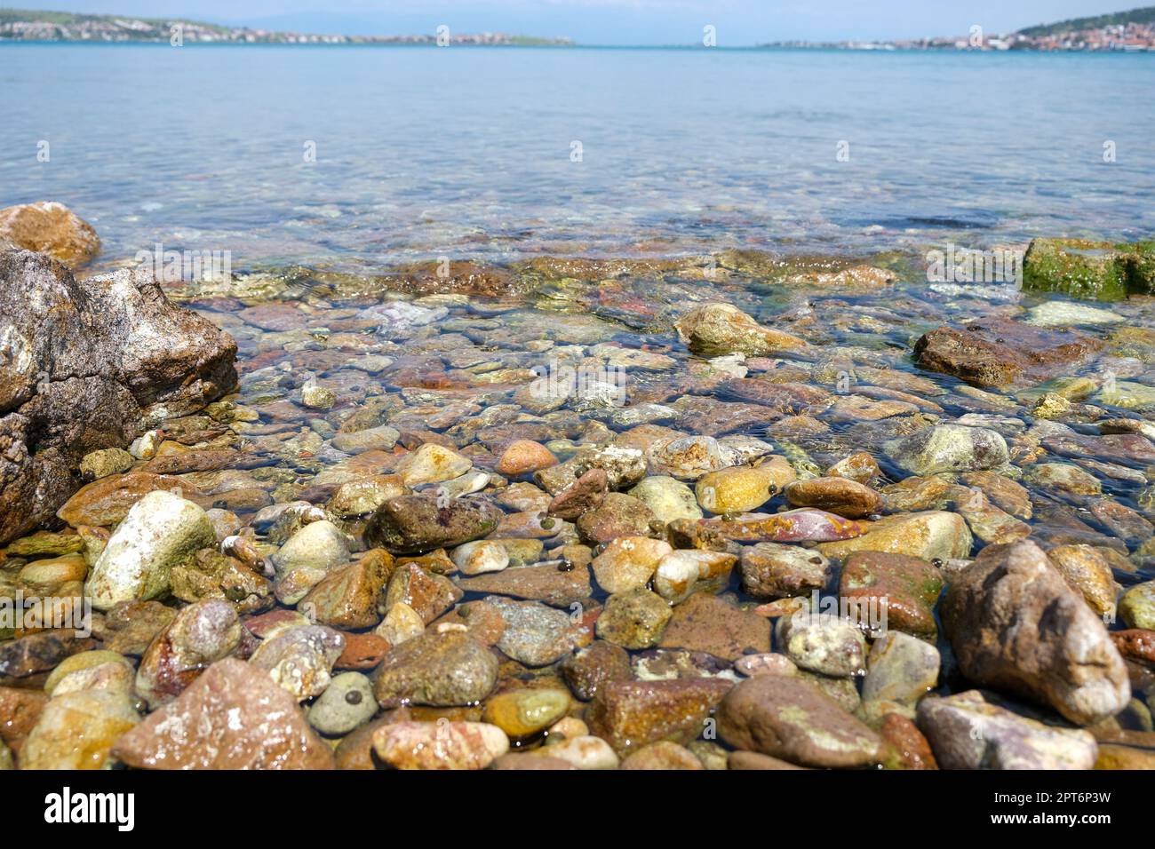 Blick vom Boden aus auf den Meeresstrand aus Kieselsteinen mit weitem Horizont und Stadt. Hintergrundkonzept für den Sommerstrand am Meer. Niemand am Strand. Stockfoto