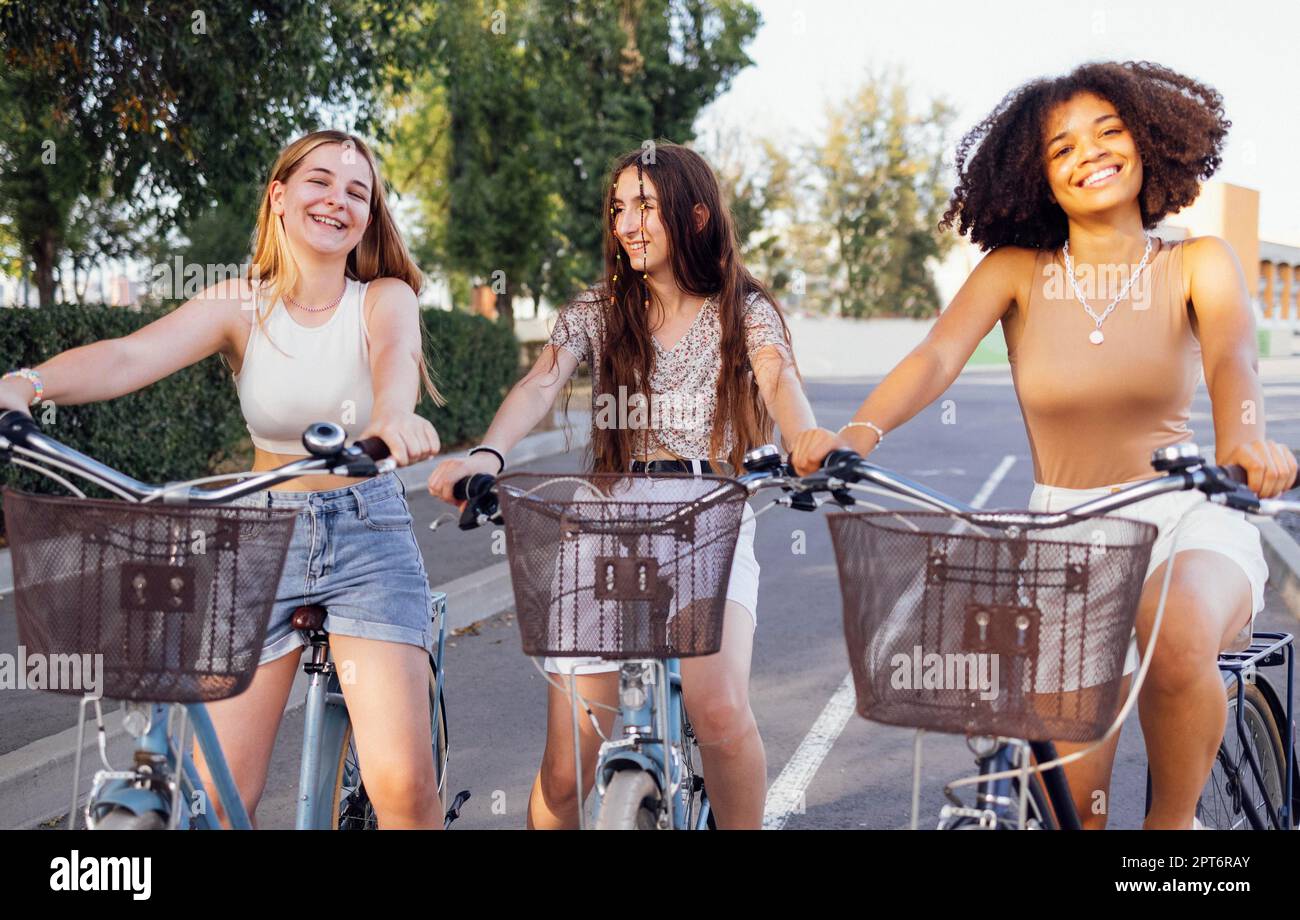 Teenager verschiedener Nationalitäten und Aussehen auf Fahrrädern fahren entlang einer Straße der Stadt. Junge und positive Mädchen lächeln zusammen. Gesunder Lebensstil Stockfoto