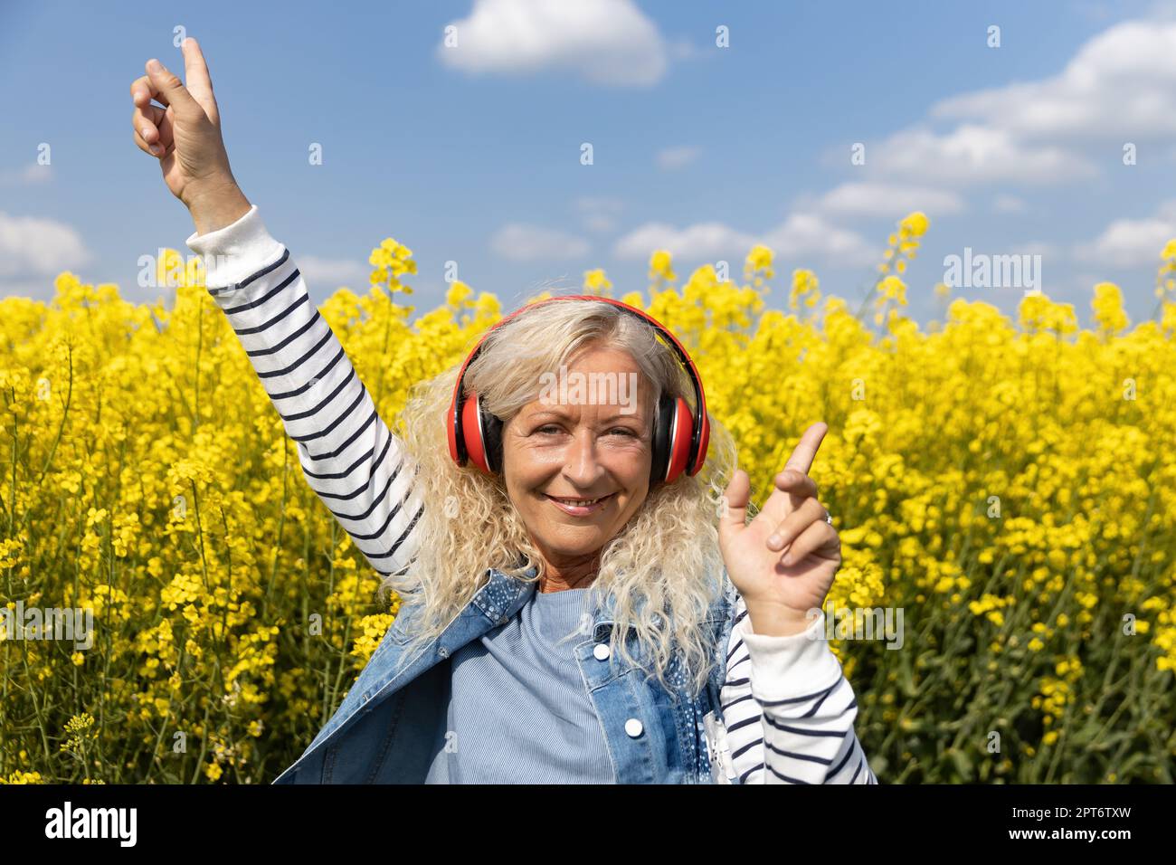 Ältere Frauen hören Musik mit Kopfhörern im blühenden Rapsfeld Stockfoto