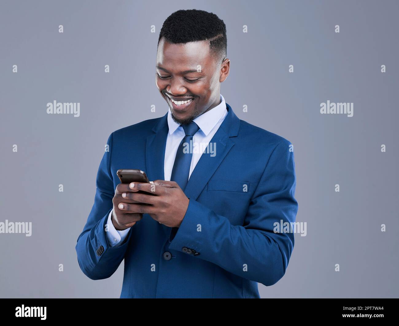 Seine Klienten müssen nie lange auf eine Antwort warten. Ein gutaussehender junger Geschäftsmann, der seine SMS im Studio vor grauem Hintergrund abliest Stockfoto