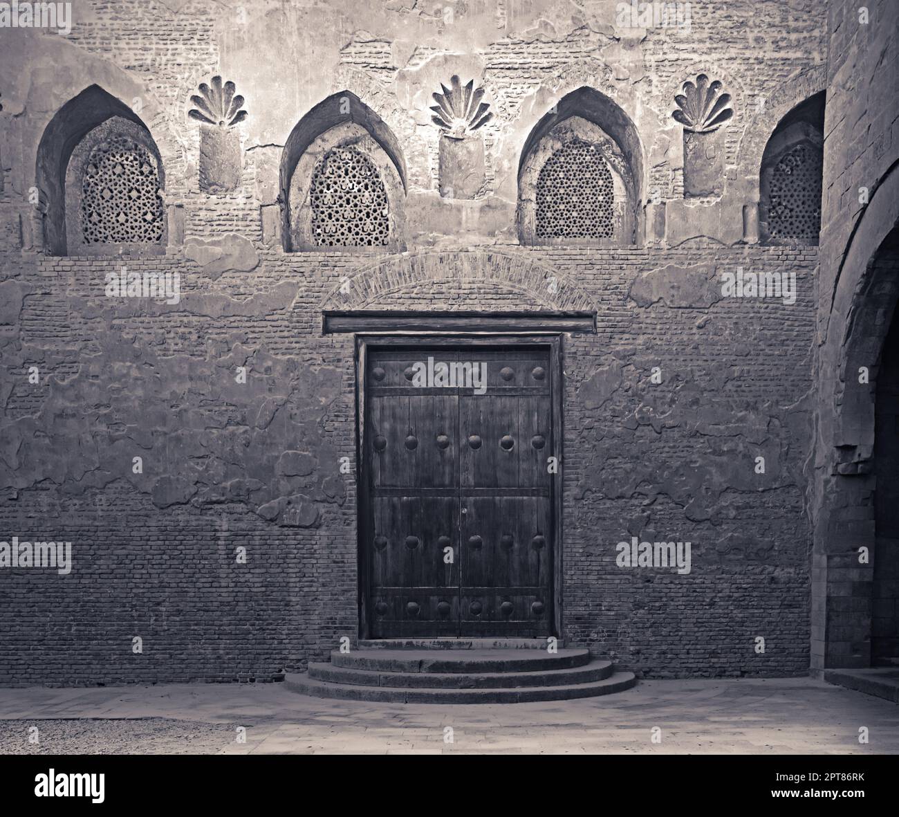 Im Alter von Holz verwitterte Tür, perforierte Gewölbte Stuckdecken Fenster mit floralen Mustern und drei Schritte auf Stein Ziegel Wand, Ibn Tulun Moschee, Ca Stockfoto